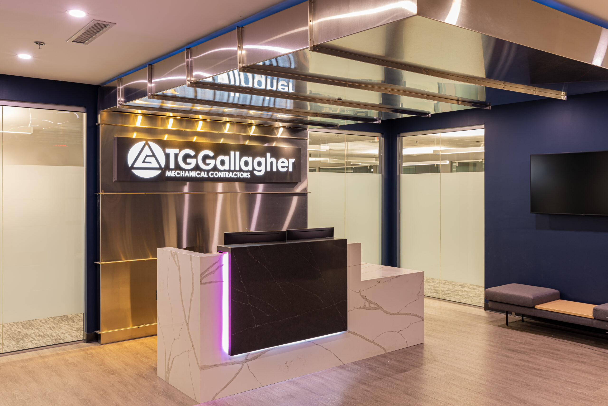 Contemporary office lobby with marble reception desk, backlit TG Gallagher sign, and glass-walled offices