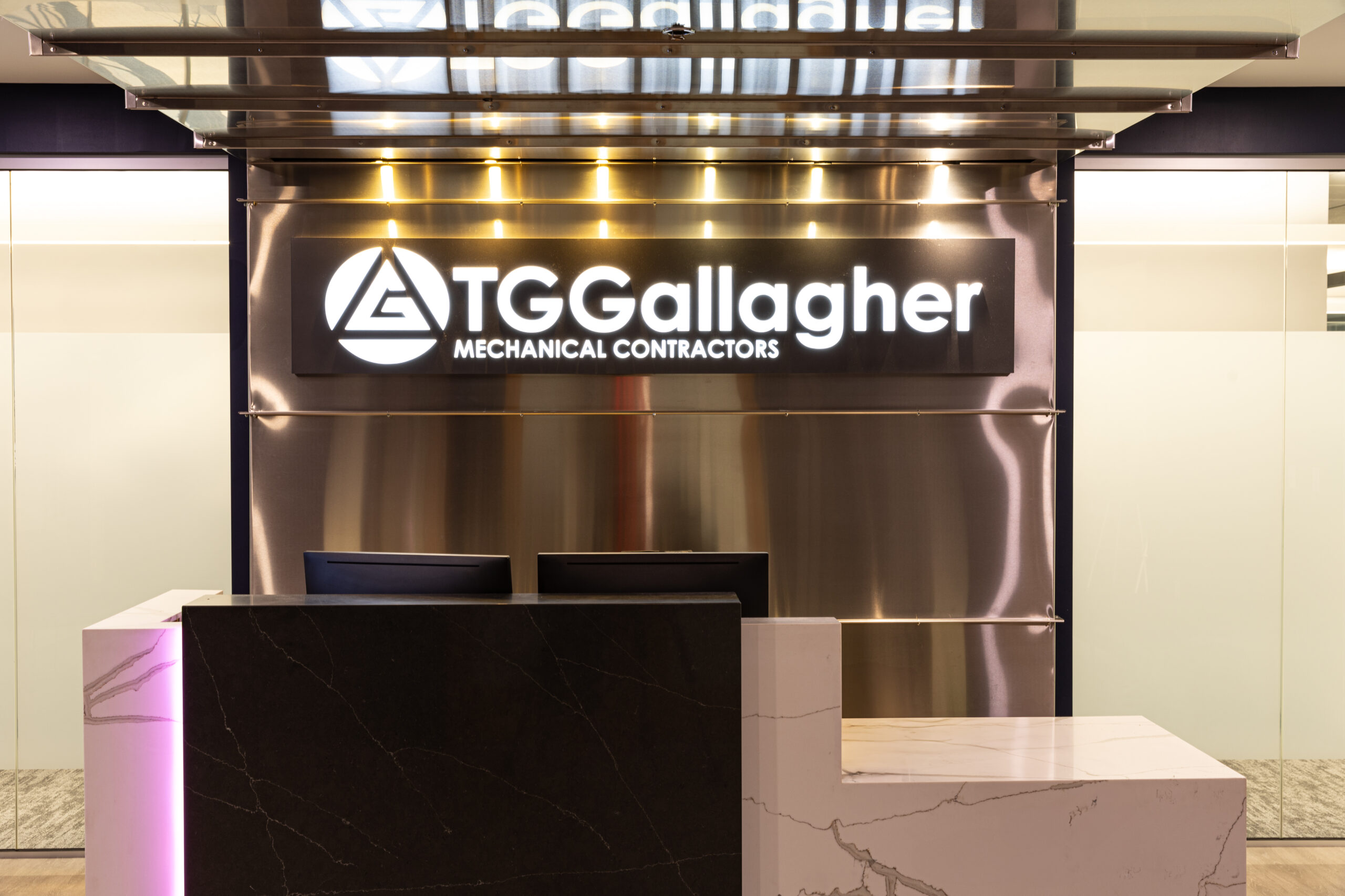 Modern reception desk with marble finishes and illuminated TG Gallagher Mechanical Contractors sign on metal backdrop