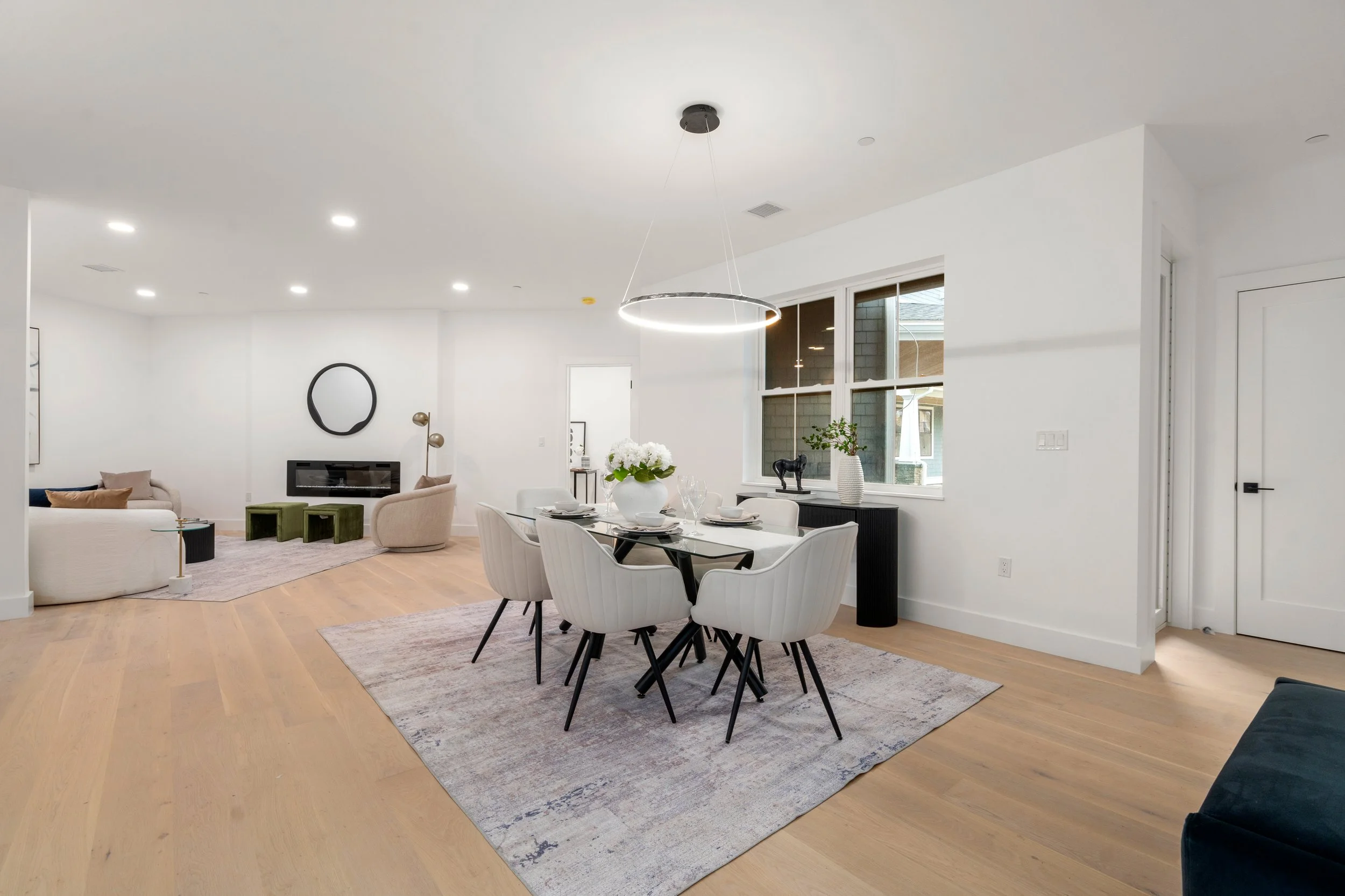 Open-plan dining and living space with modern table, lounge seating, and wall-mounted fireplace
