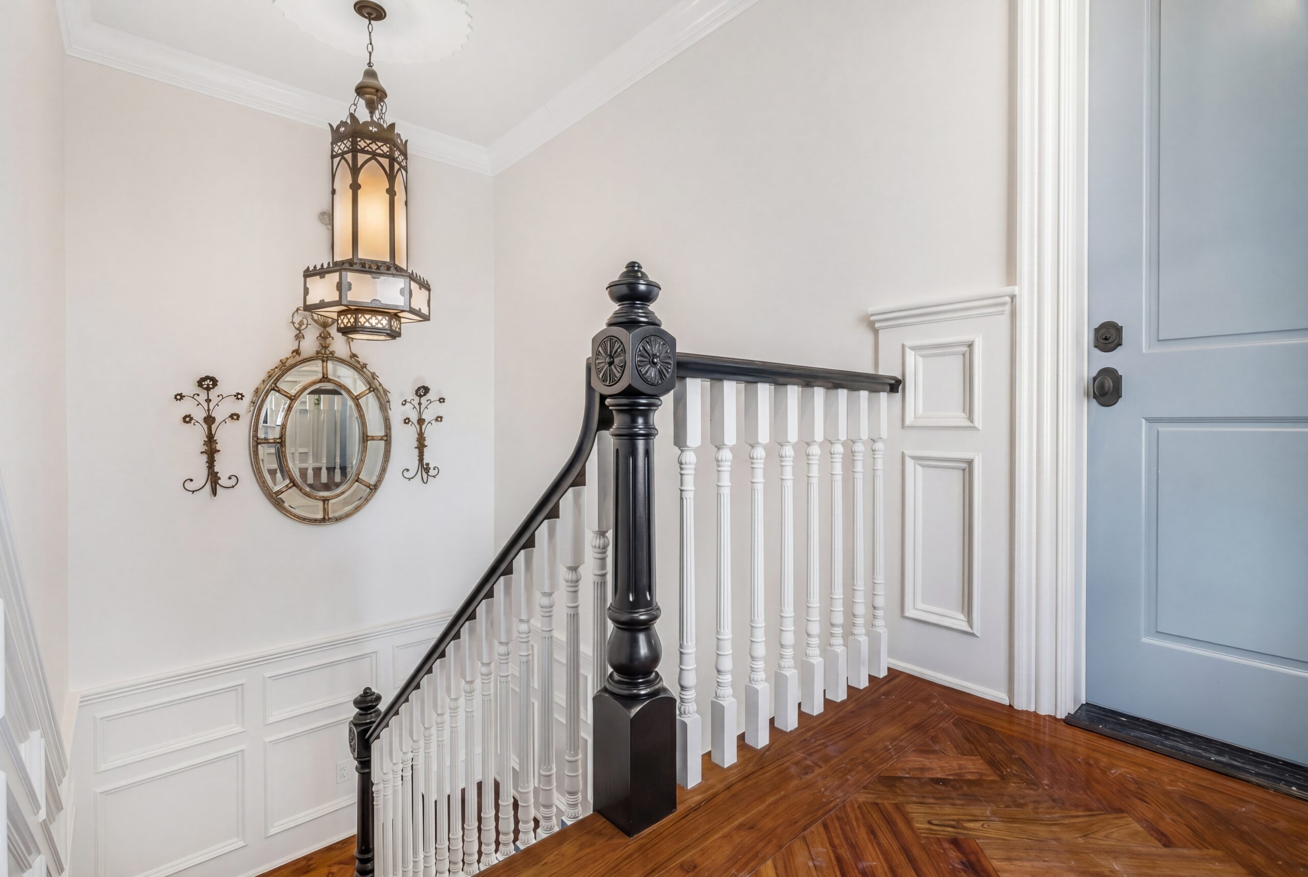 Entry stair with wood herringbone floor, white balustrade, black newel post, and hanging lantern light
