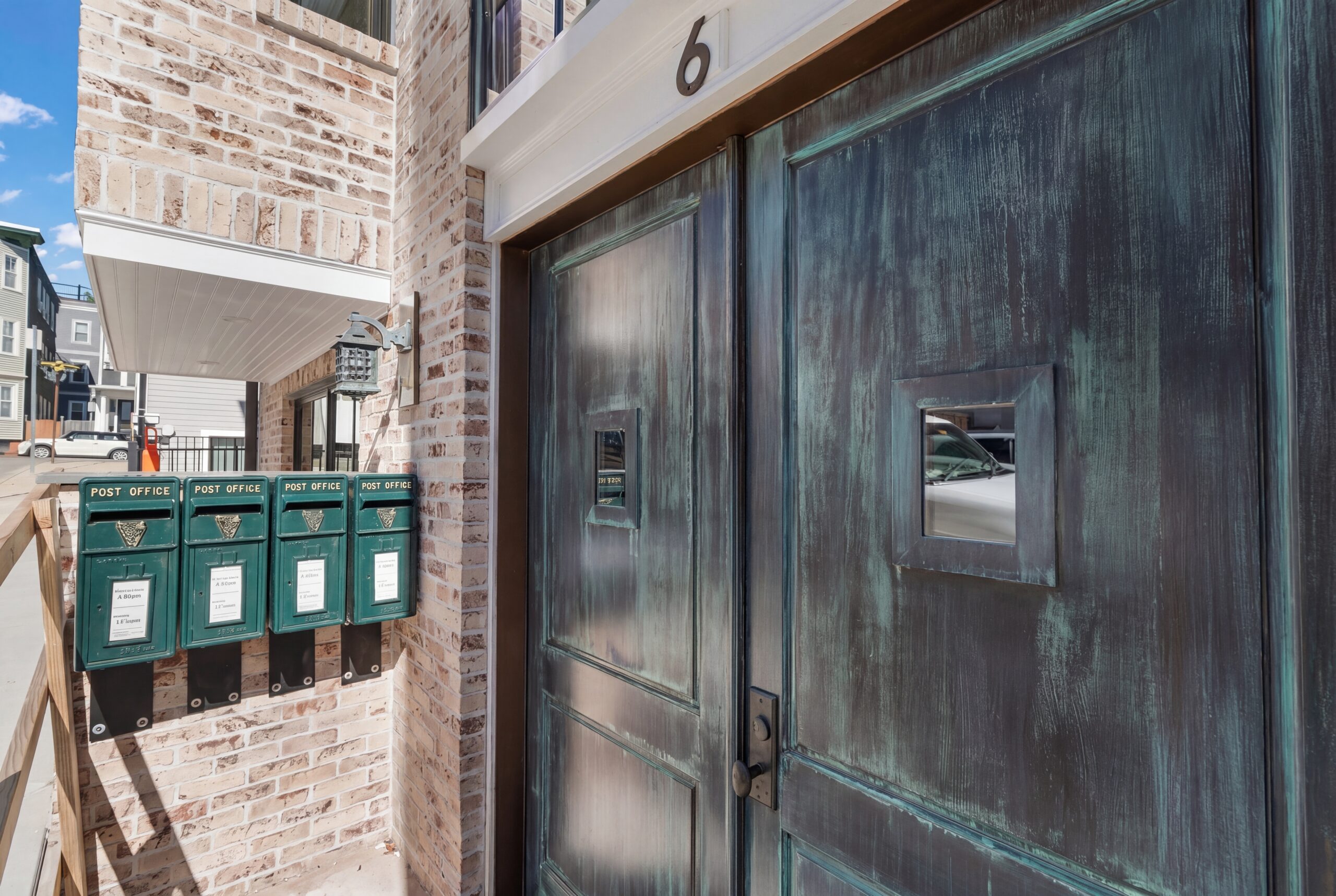 Brick building entrance with patina-finished metal doors, wall-mounted mailboxes, and exterior lighting