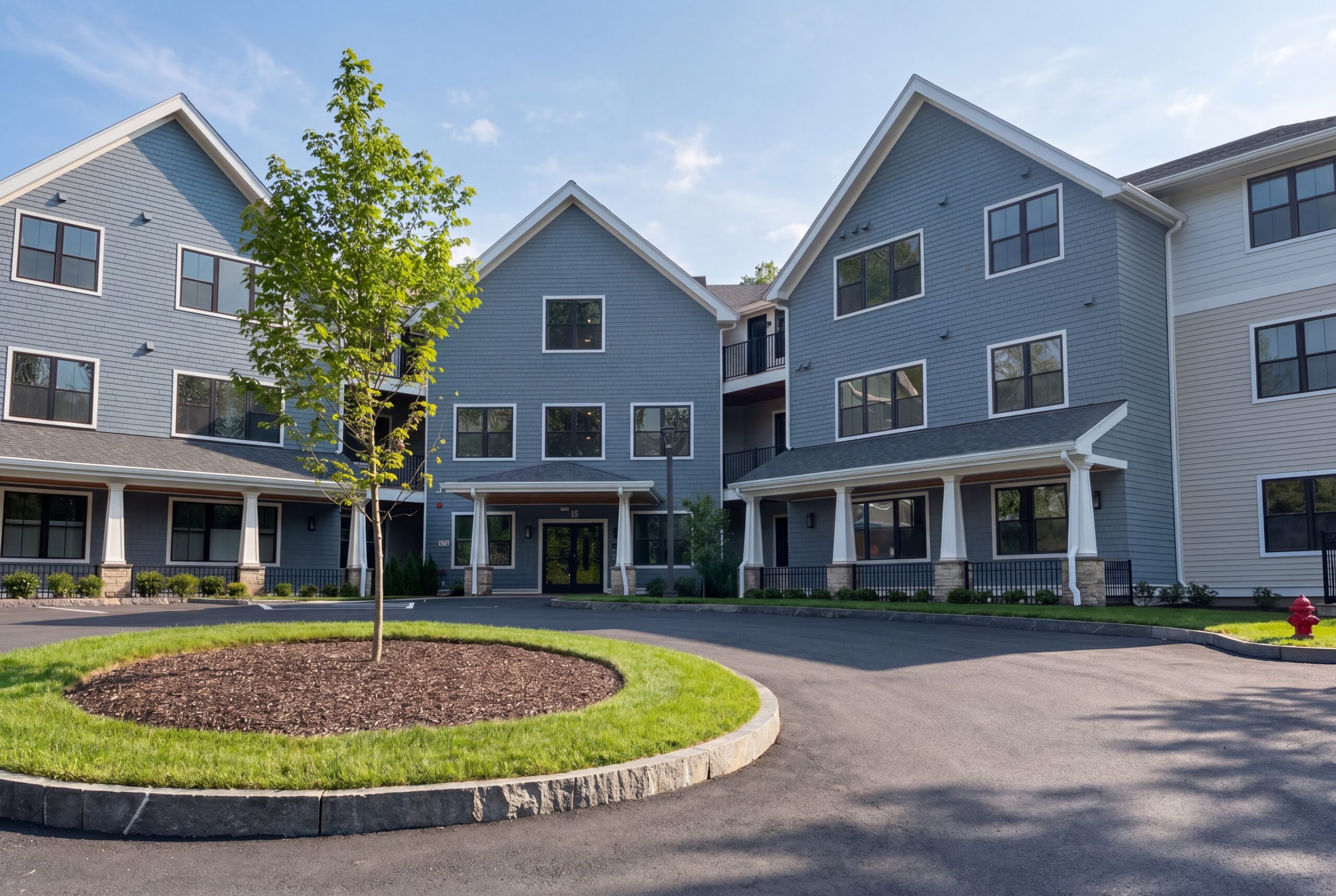 Three-story multi-family building with gabled roofs, covered entries, and landscaped circular drive
