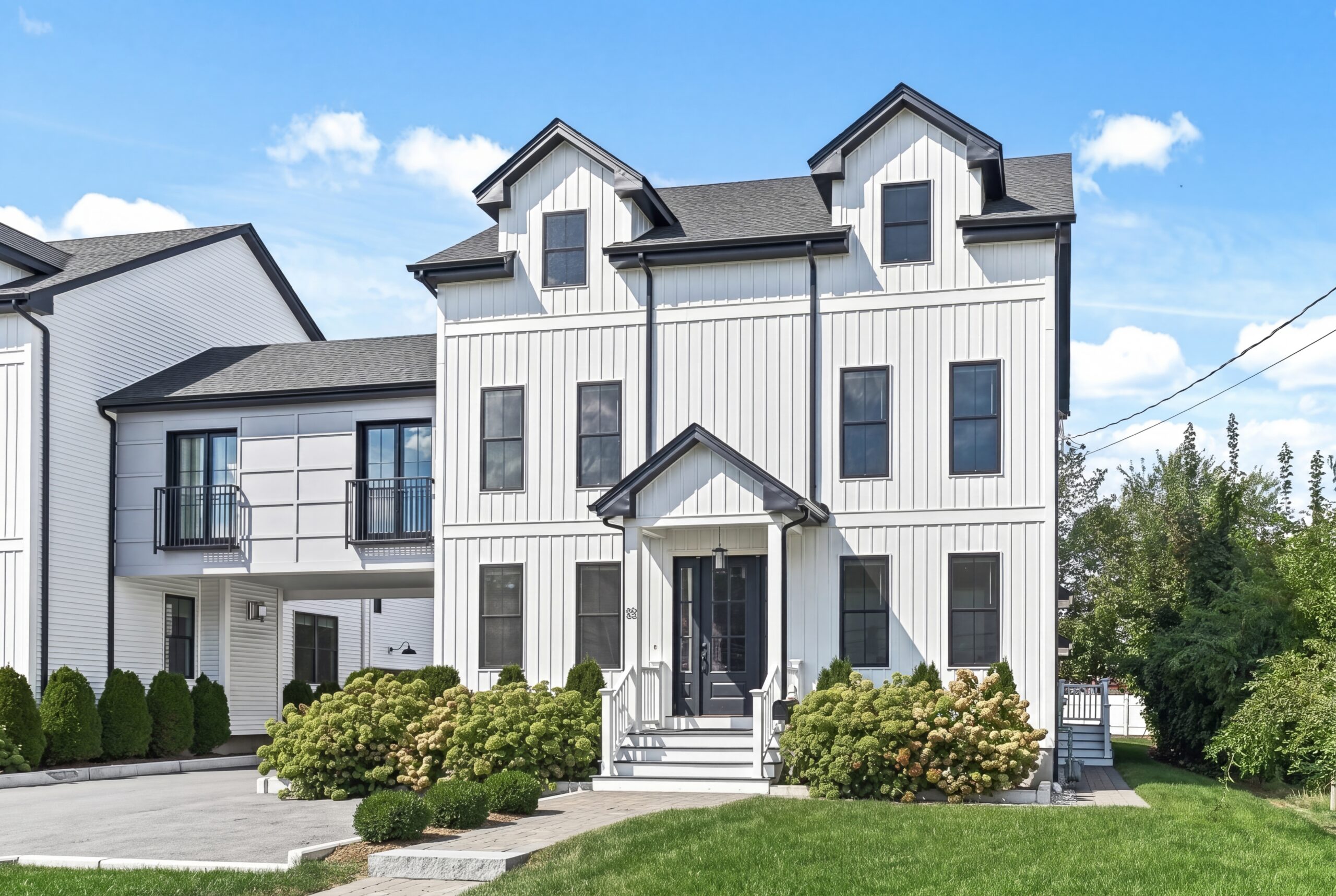 Modern farmhouse exterior with white vertical siding, black-framed windows, symmetrical façade, and landscaped front yard with hydrangeas and clean entry approach<br />
