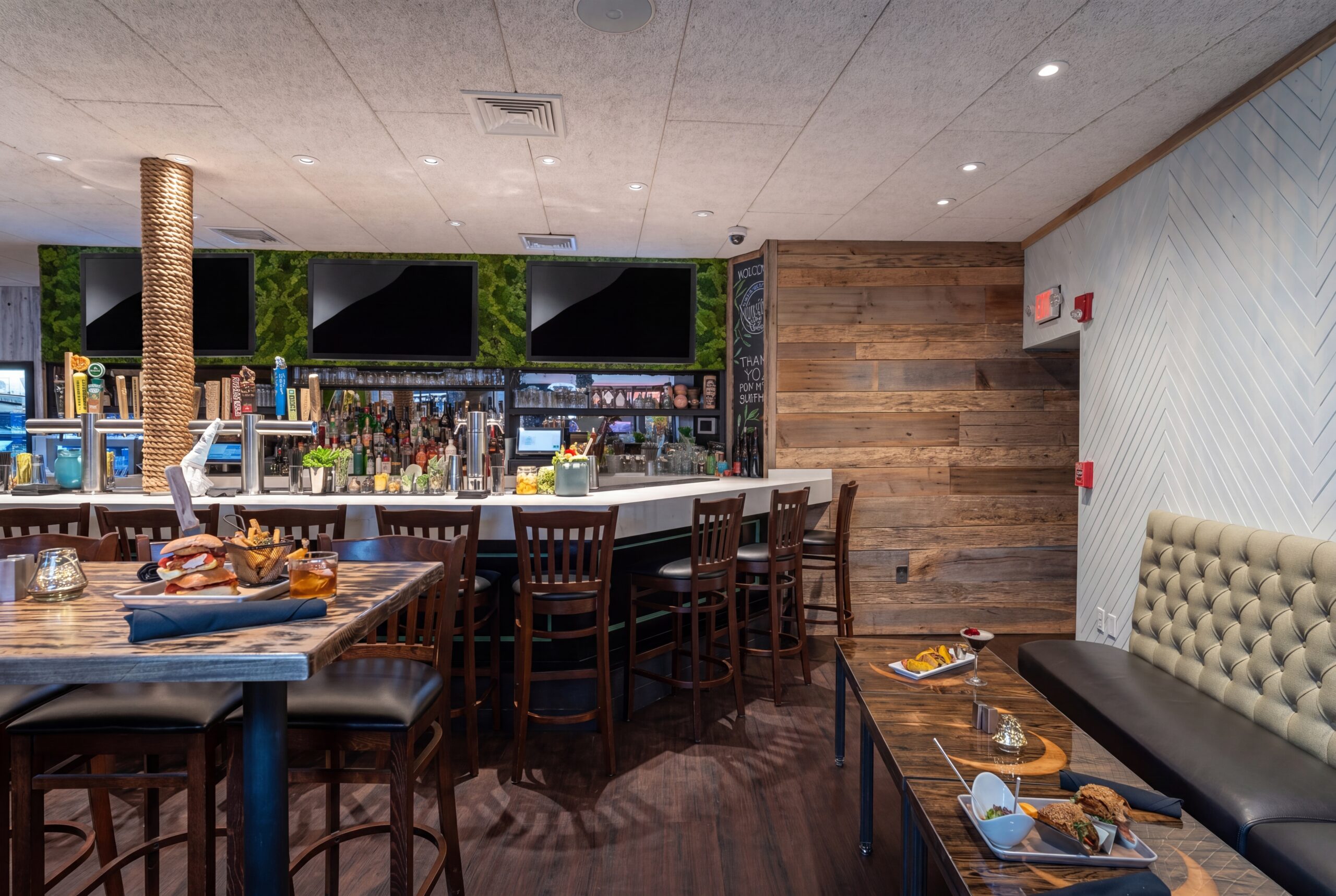 Lively bar area with wood seating, craft beer taps, and a full back bar, complemented by warm finishes, tufted banquette seating, and a vibrant social atmosphere<br />
