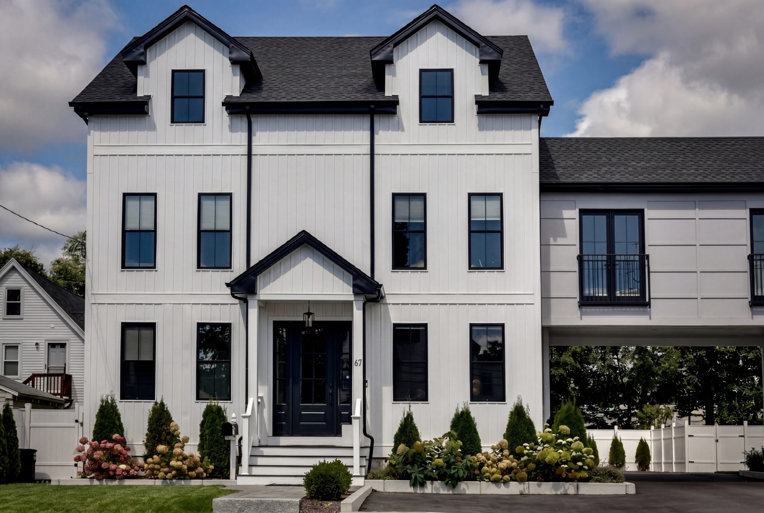 Modern farmhouse exterior with white vertical siding, black windows, gabled rooflines, and landscaped front entry with symmetrical plantings