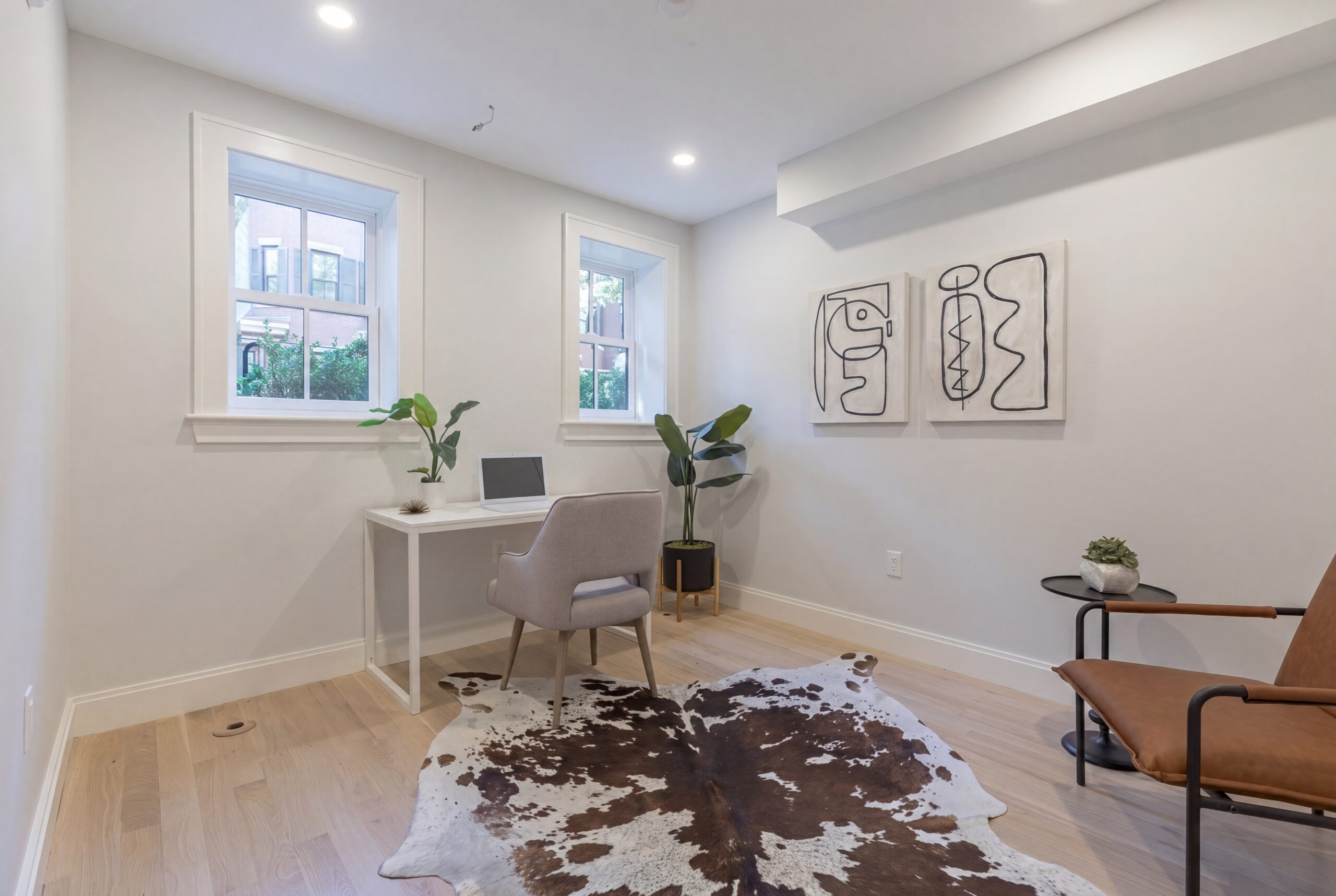 Contemporary home office interior within a renovated Boston row house, featuring a minimalist workspace with soft neutral finishes, light oak flooring, modern furnishings, and clean-lined contemporary artwork. Natural daylight filters through traditional windows, creating a bright and functional flex space designed for modern urban living.<br />
