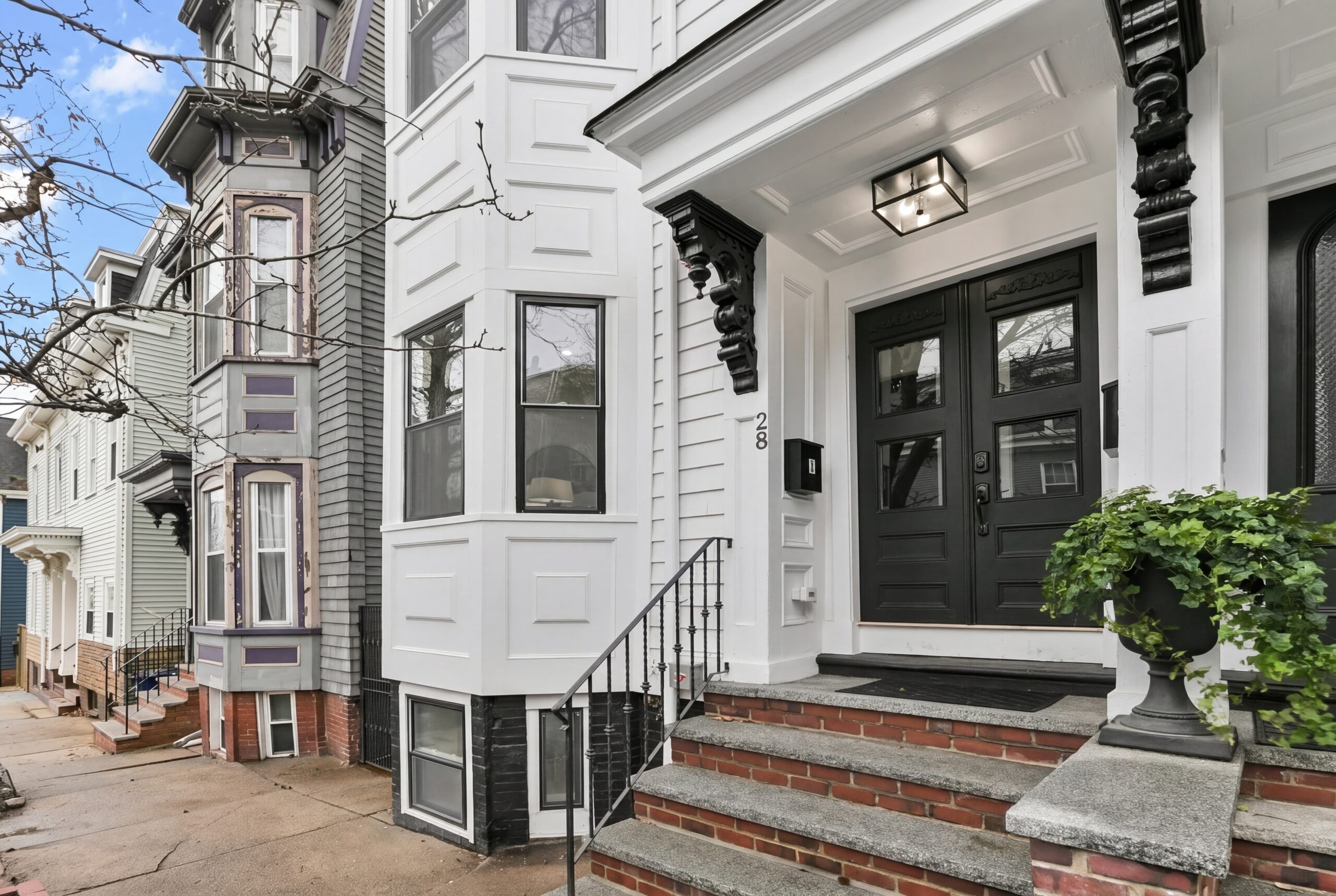 Restored South Boston single family home renovated after fire damage with modern black entry doors, detailed white facade, and updated bay windows.