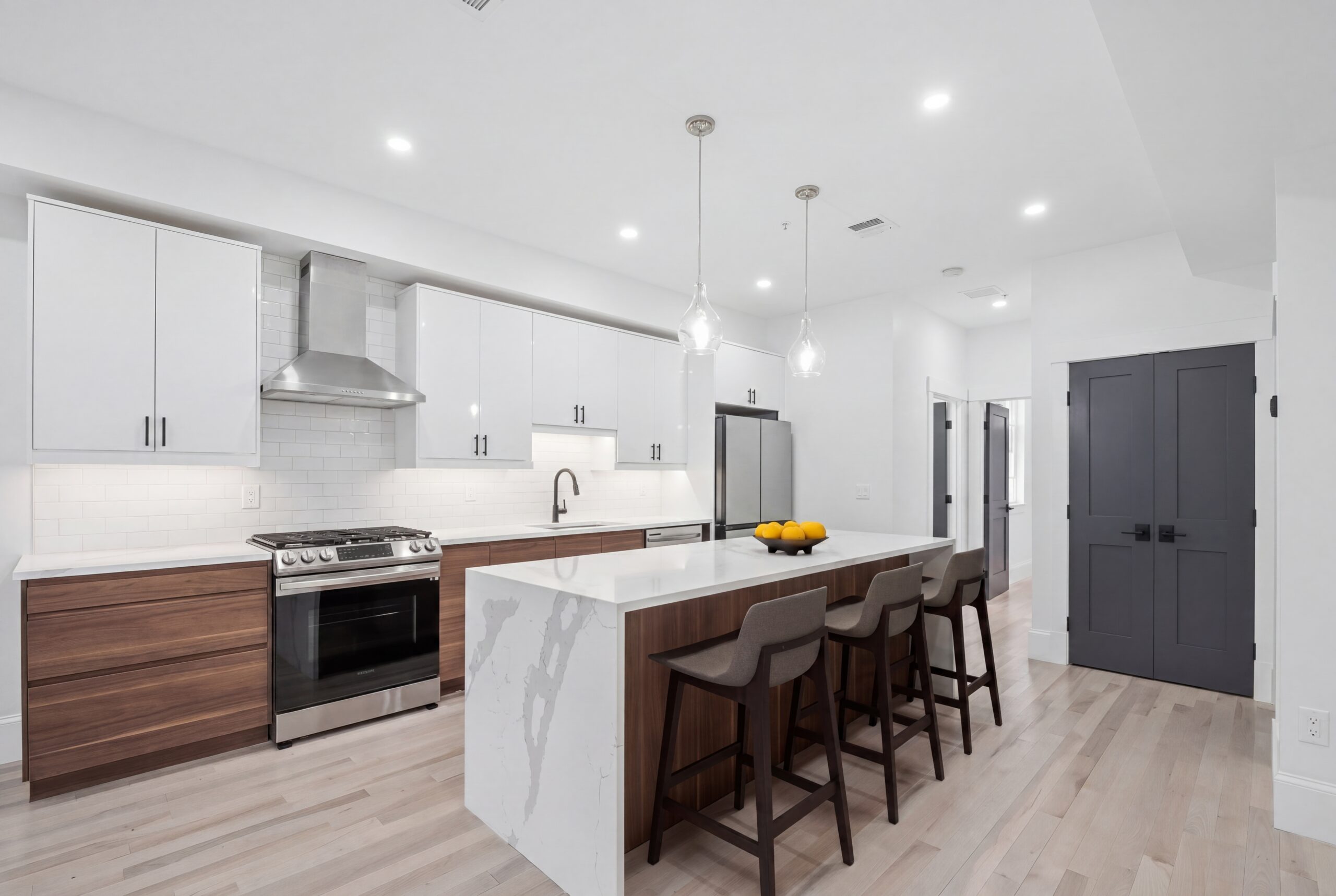 Modern South Boston single family kitchen renovation with waterfall quartz island, custom wood cabinetry, white upper cabinets, and contemporary black accents.