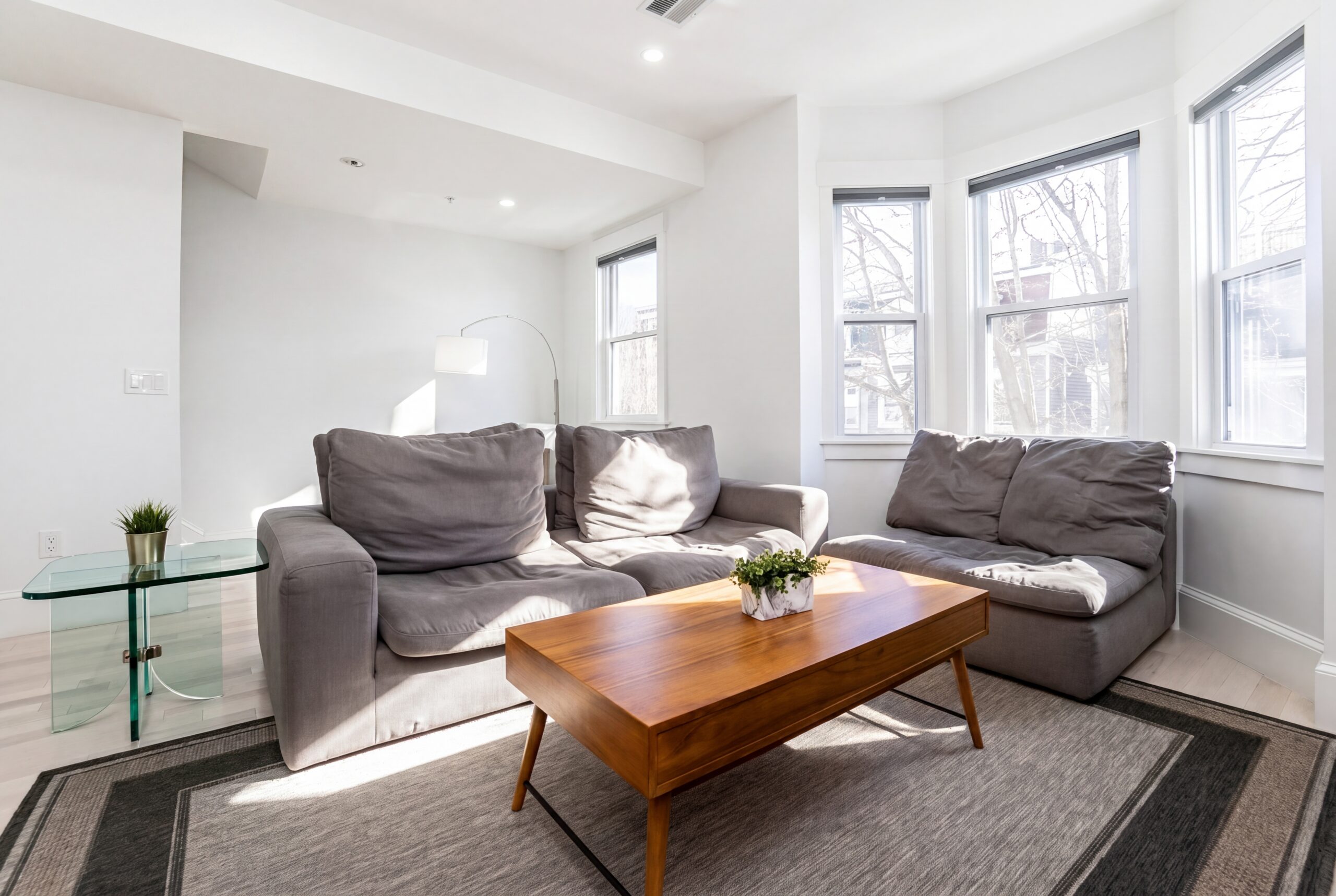 Bright contemporary living room in a renovated South Boston multifamily home featuring bay windows, natural light, and modern minimalist interiors.<br />
