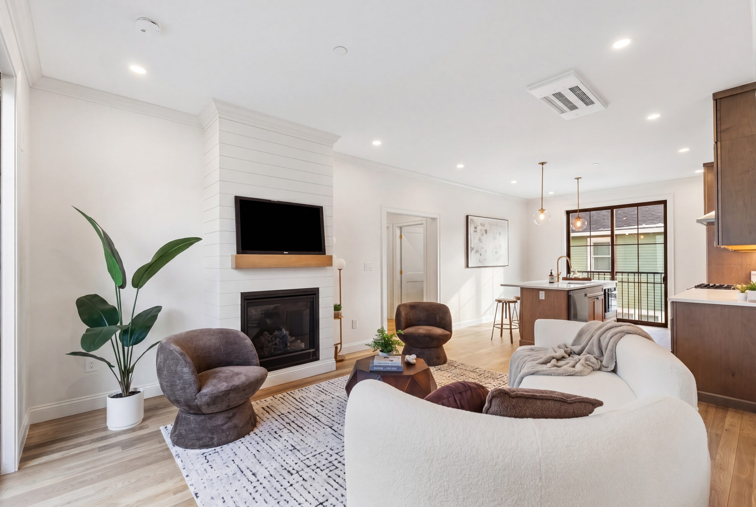 Modern open-concept living room and kitchen in Boston multifamily residence featuring fireplace, natural wood cabinetry, and contemporary finishes<br />
