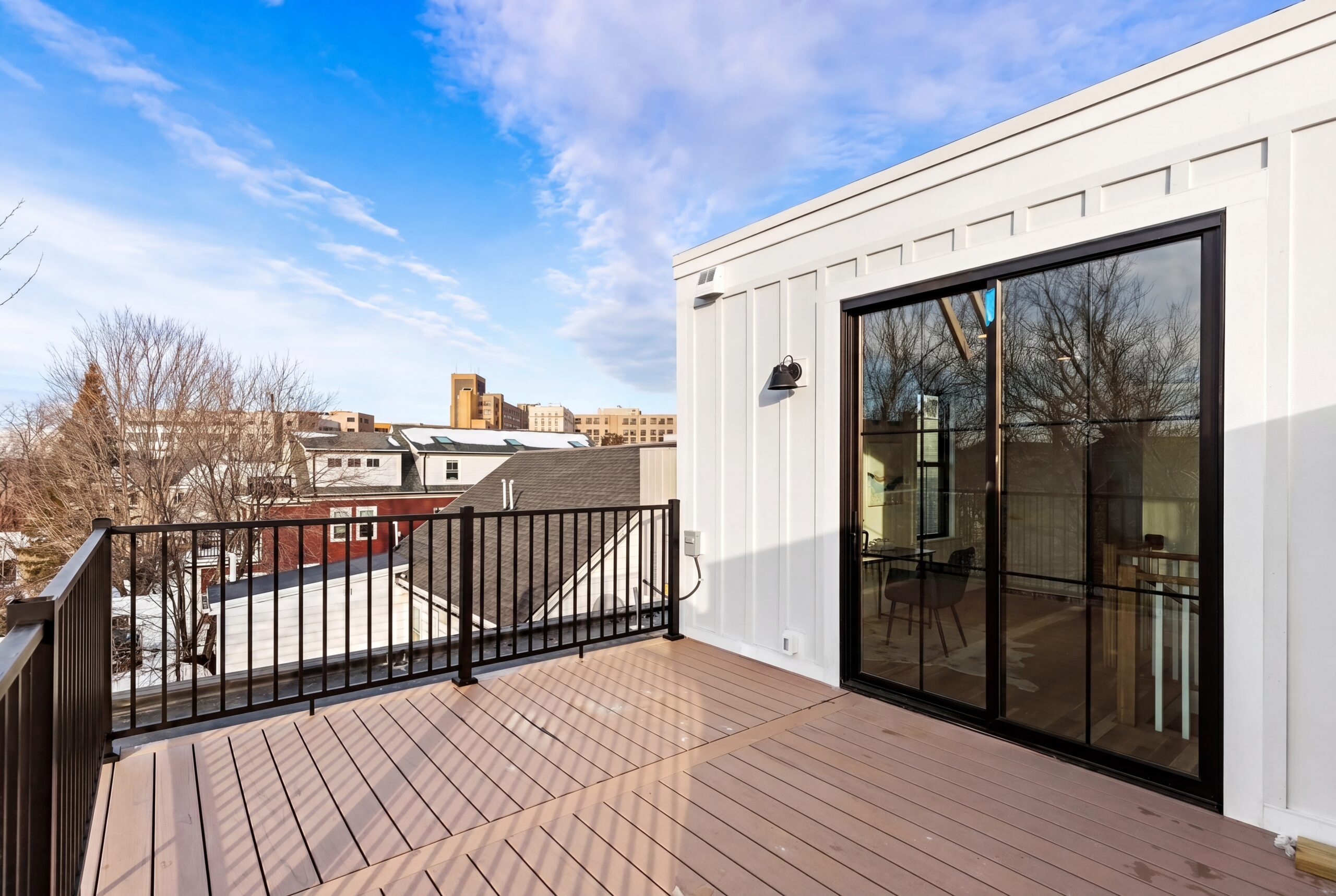 Modern rooftop terrace in Boston multifamily residence with composite decking, black railings, and sliding glass doors overlooking the city skyline<br />
