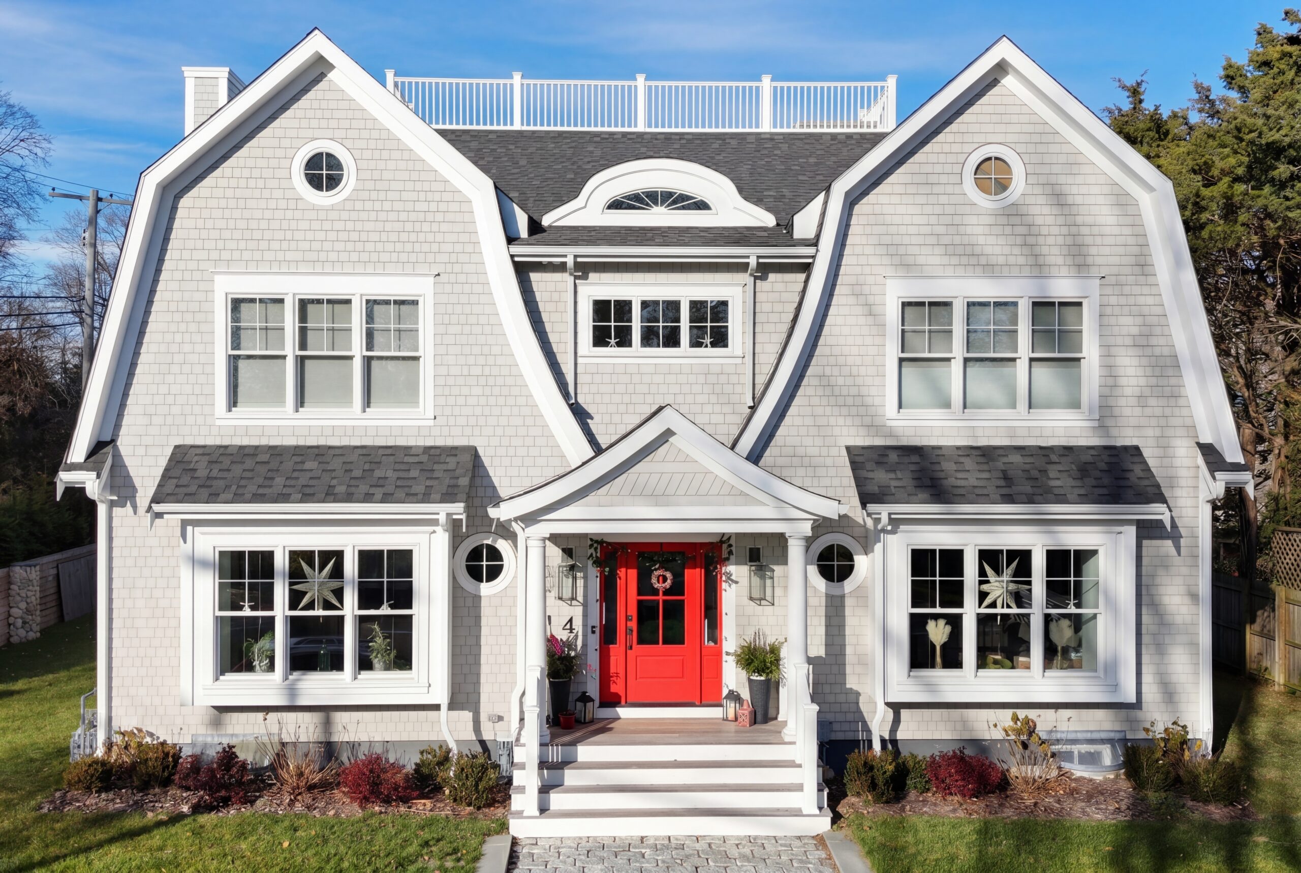 Coastal-inspired single-family home with gambrel roofs, rooftop deck, and symmetrical shingle-style façade featuring a bold red entry door