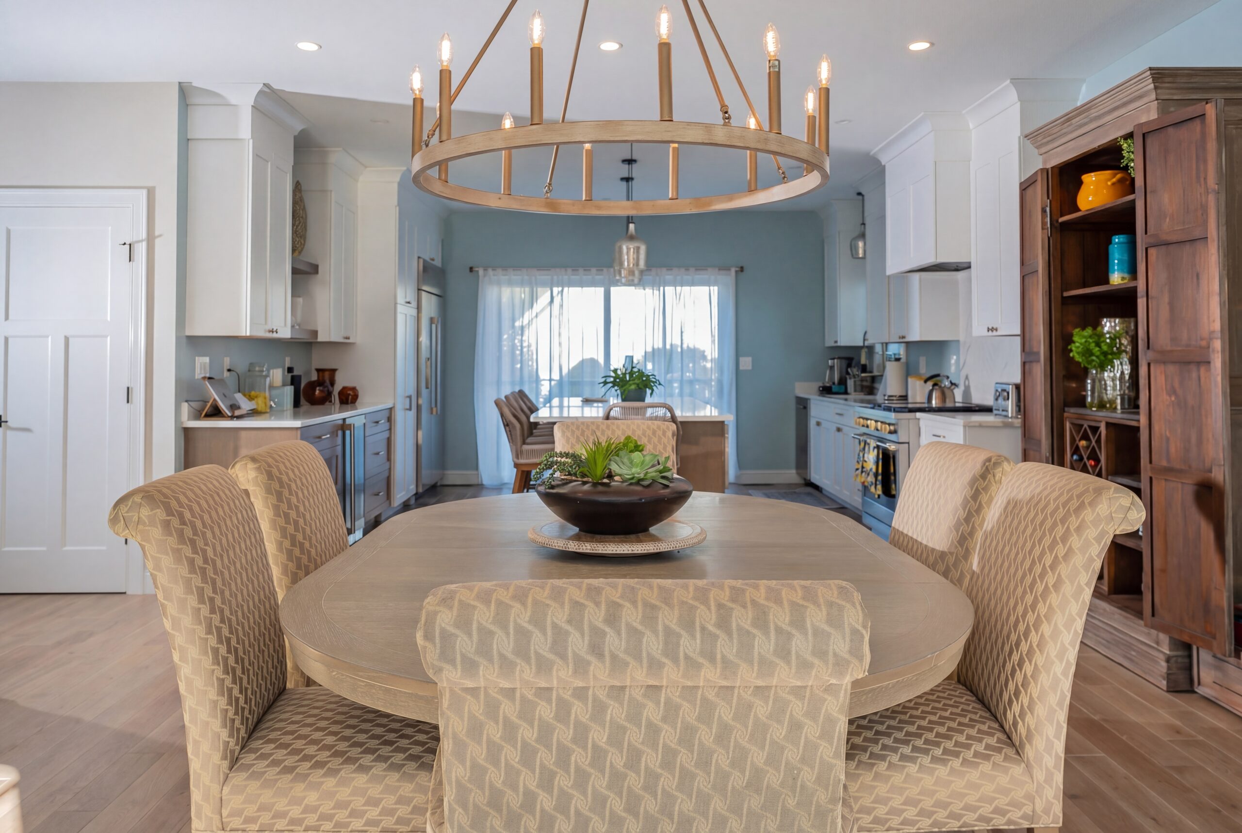 Contemporary dining room and kitchen with custom millwork, oversized chandelier, and warm transitional finishes in a coastal-inspired residence<br />
