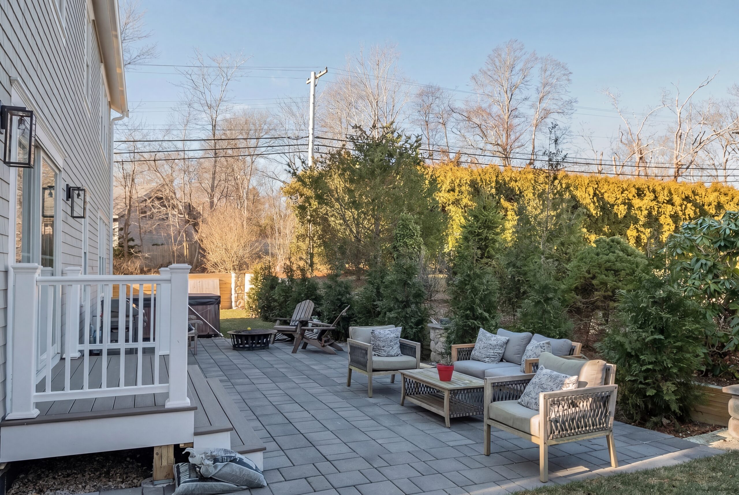 Coastal-inspired backyard patio with outdoor lounge seating, landscaped privacy screening, and modern deck access at a single-family residence<br />
