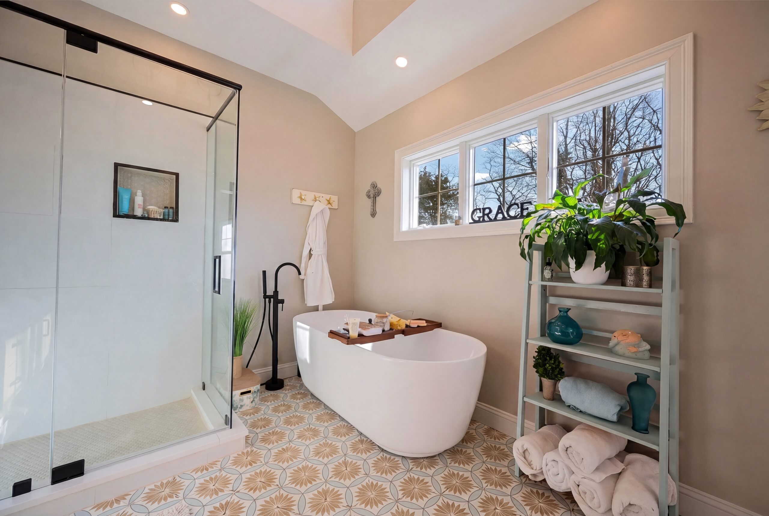 Contemporary spa-style bathroom with freestanding soaking tub, walk-in glass shower, and patterned tile flooring in a coastal-inspired residence<br />
