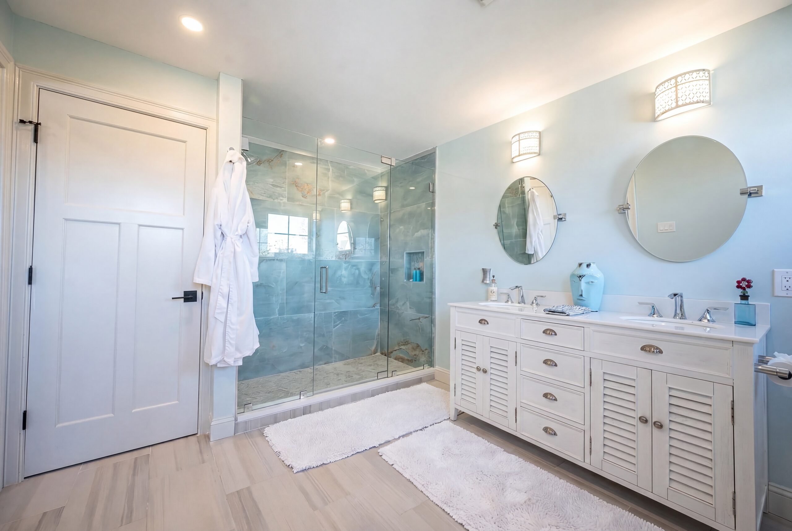 Coastal-inspired primary bathroom with double vanity, oversized glass shower, and soft blue spa-like finishes in a luxury single-family residence<br />
