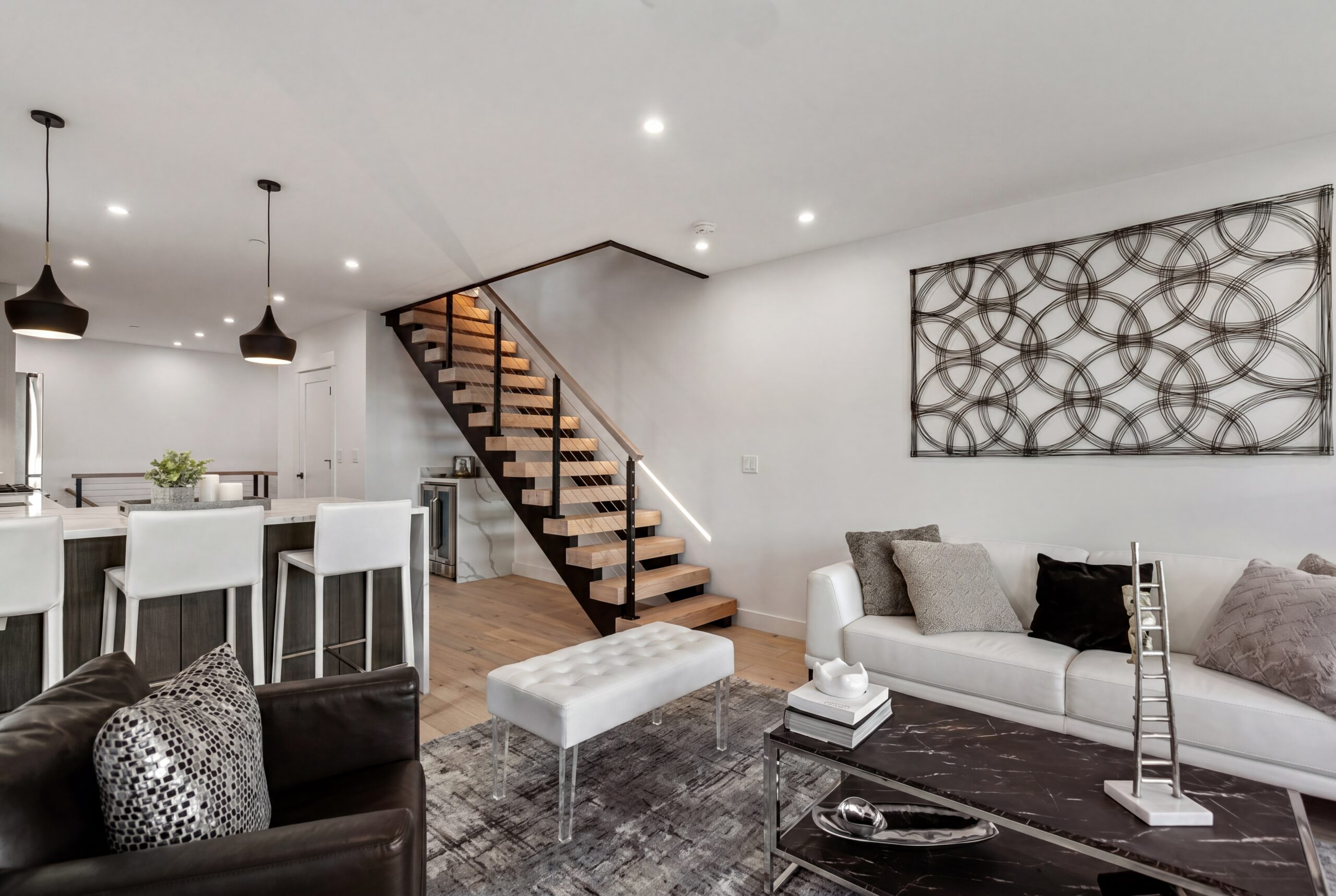 Athens Street_Open Concept Contemporary open-concept living interior within a modern multifamily residence, featuring floating wood stair treads with glass railings, minimalist finishes, and a refined neutral material palette. The space combines a sleek modern kitchen, integrated lighting, and contemporary furnishings to create a bright and sophisticated urban living environment designed for modern city living.<br />
