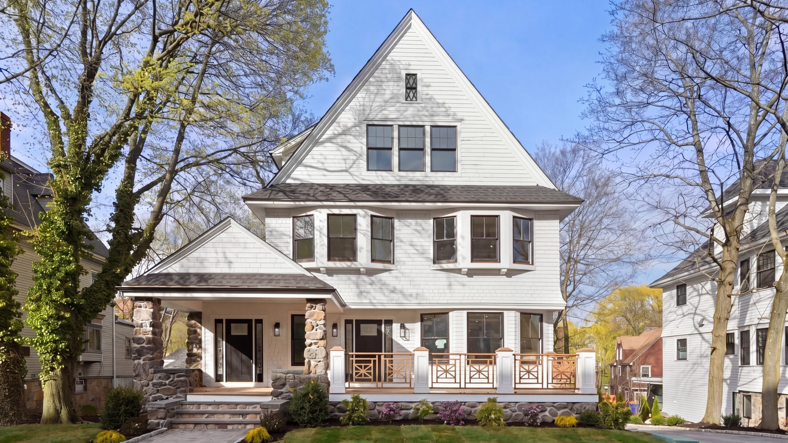 Three-story white clapboard house with gabled roof, stone-columned porch, and front deck with wood railings