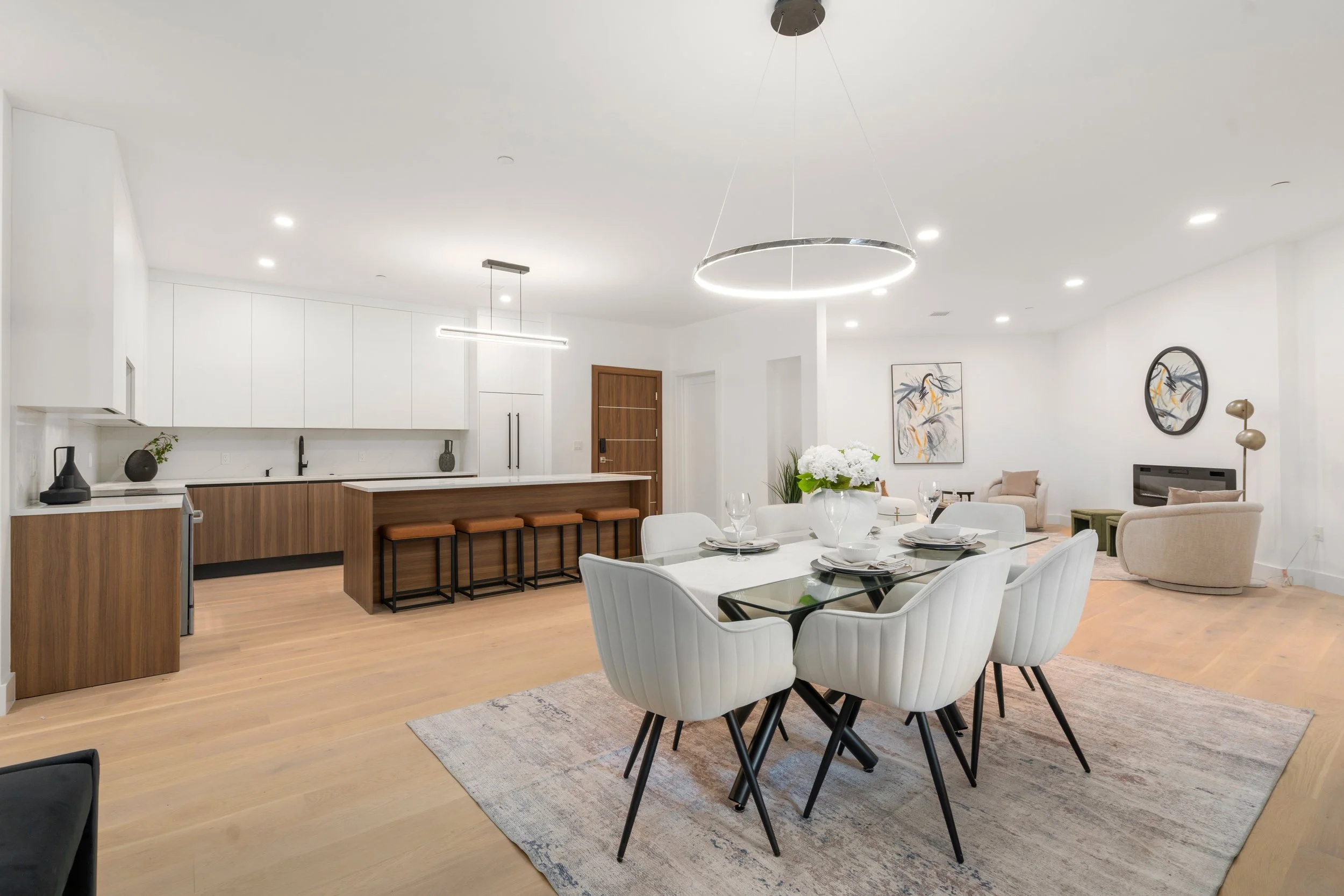 Open-plan dining and kitchen with large island, modern lighting fixtures, and seating area beyond