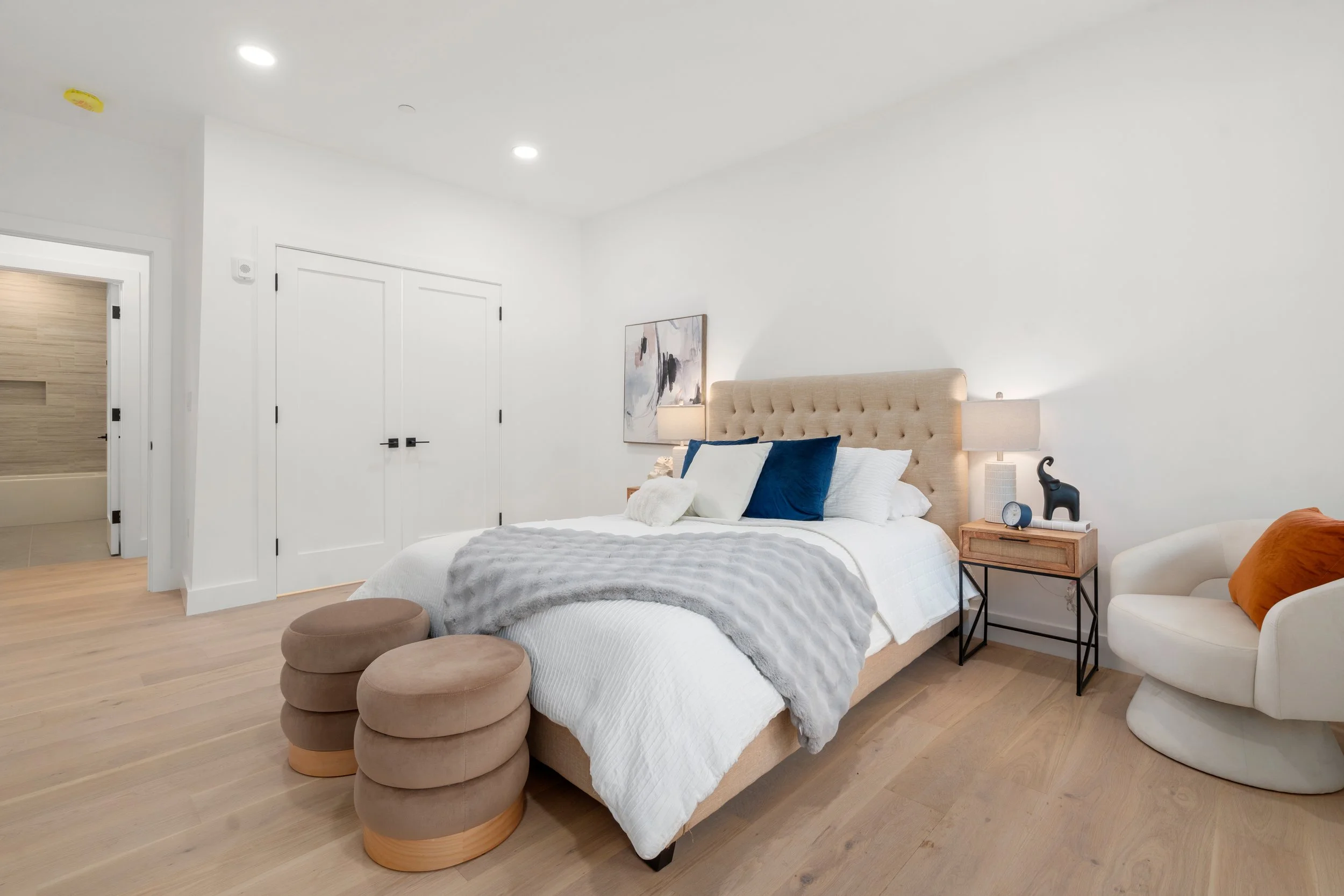 Bright bedroom with upholstered bed, neutral bedding, bedside tables, and seating area