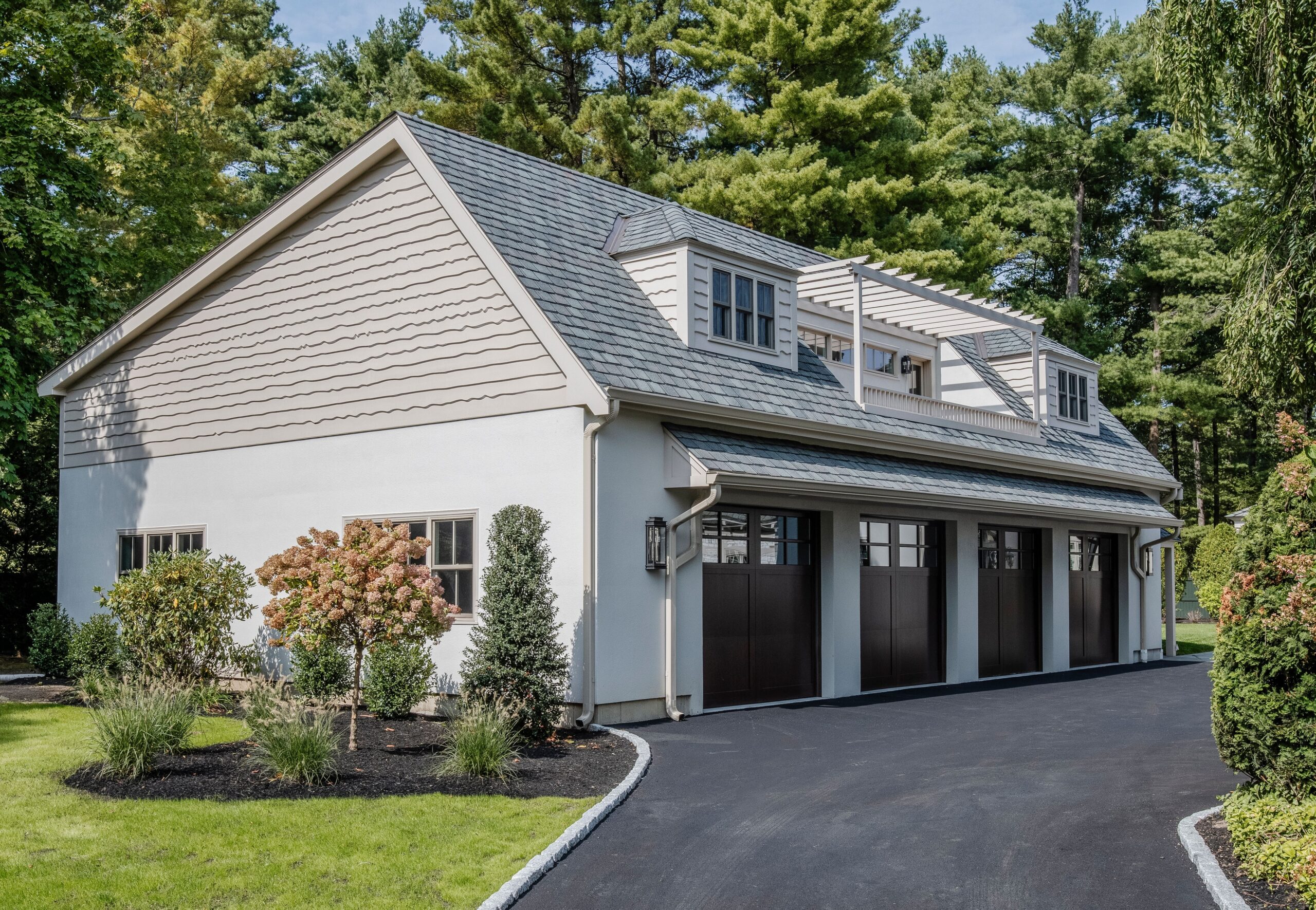 Coastal-inspired detached garage and guest house with gambrel rooflines, pergola terrace, and carriage-style garage doors surrounded by landscaped grounds
