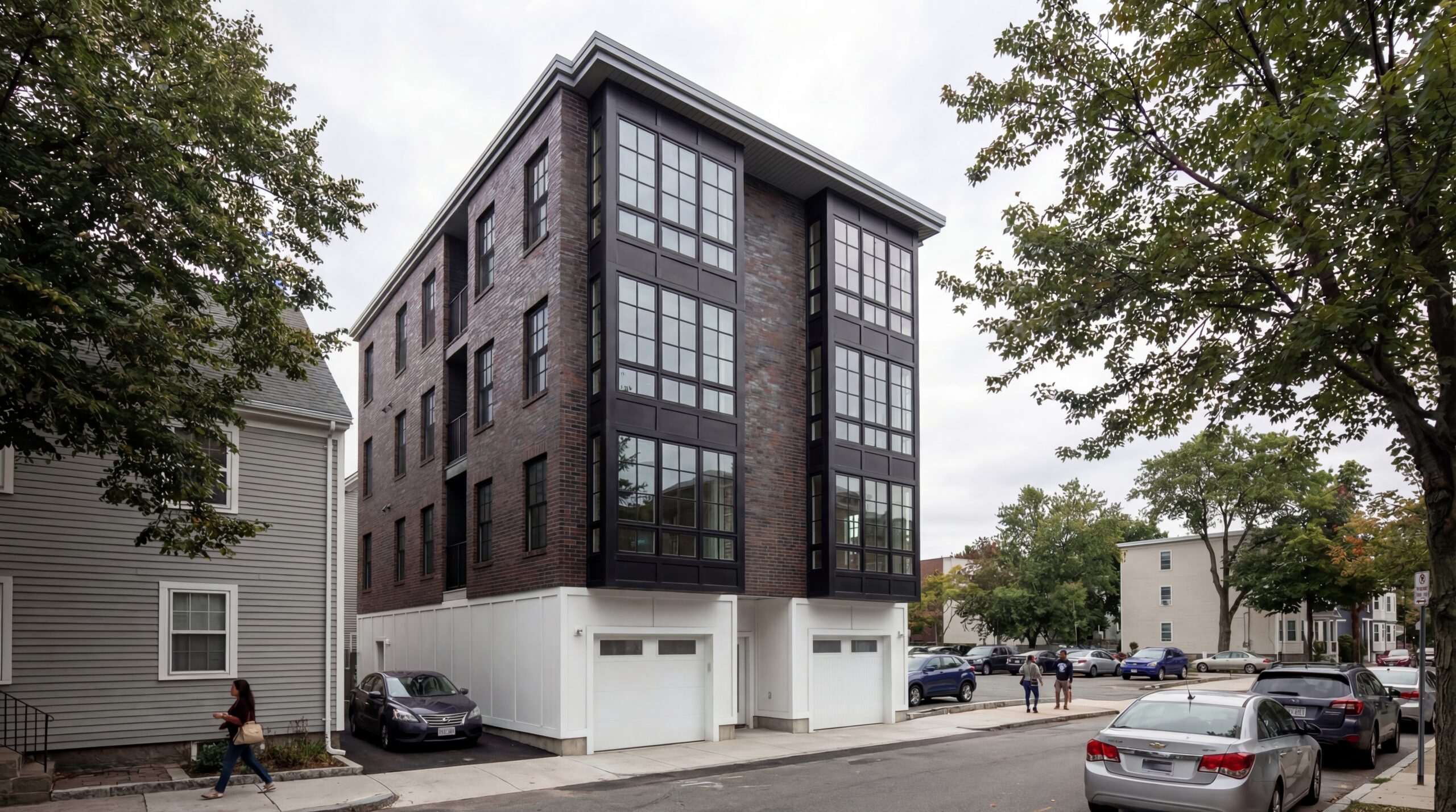 Athens St-Exterior Contemporary multifamily residential building featuring a dark brick façade, expansive black-framed window walls, and modern urban detailing within a dense neighborhood streetscape. The four-story development combines clean contemporary forms with warm masonry materials, integrated garage access, and large vertical glazing elements that create a bold architectural presence against the surrounding residential context.<br />