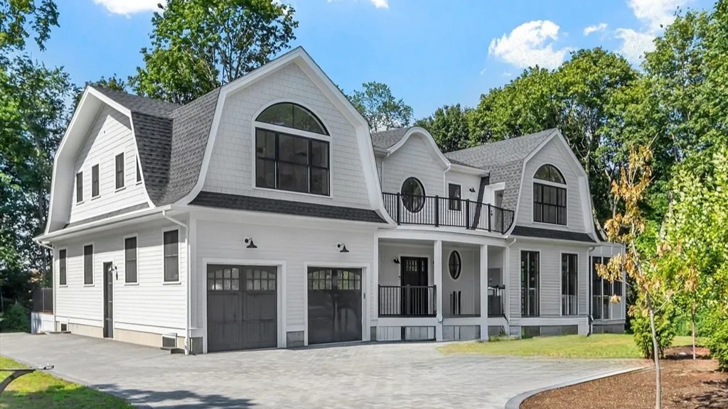 Luxury single-family residence featuring coastal-inspired architecture, curved gambrel rooflines, expansive windows, covered front porch, second-floor terrace, and a three-car garage on a landscaped estate property.