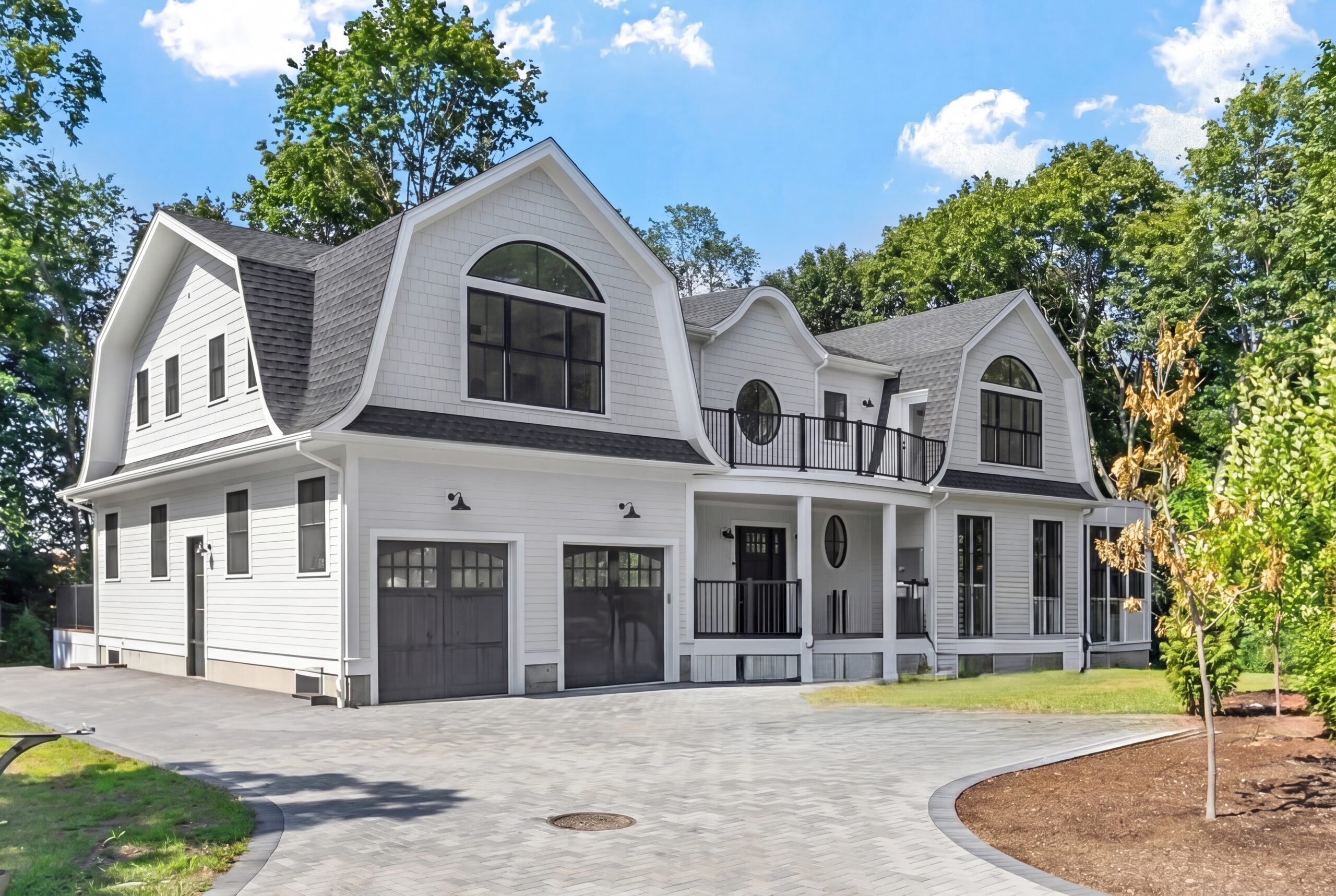 Luxury single-family residence featuring coastal-inspired architecture, curved gambrel rooflines, expansive windows, covered front porch, second-floor terrace, and a three-car garage on a landscaped estate property.