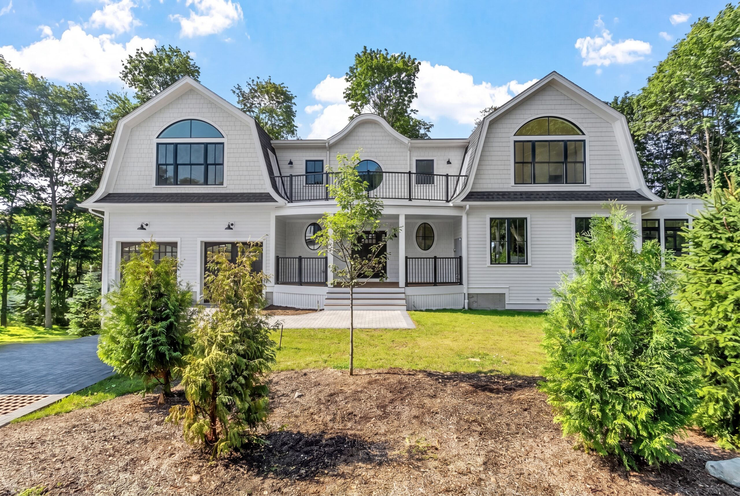 Luxury single-family residence featuring coastal-inspired architecture, curved gambrel rooflines, expansive windows, covered front porch, second-floor terrace, and a three-car garage on a landscaped estate property.