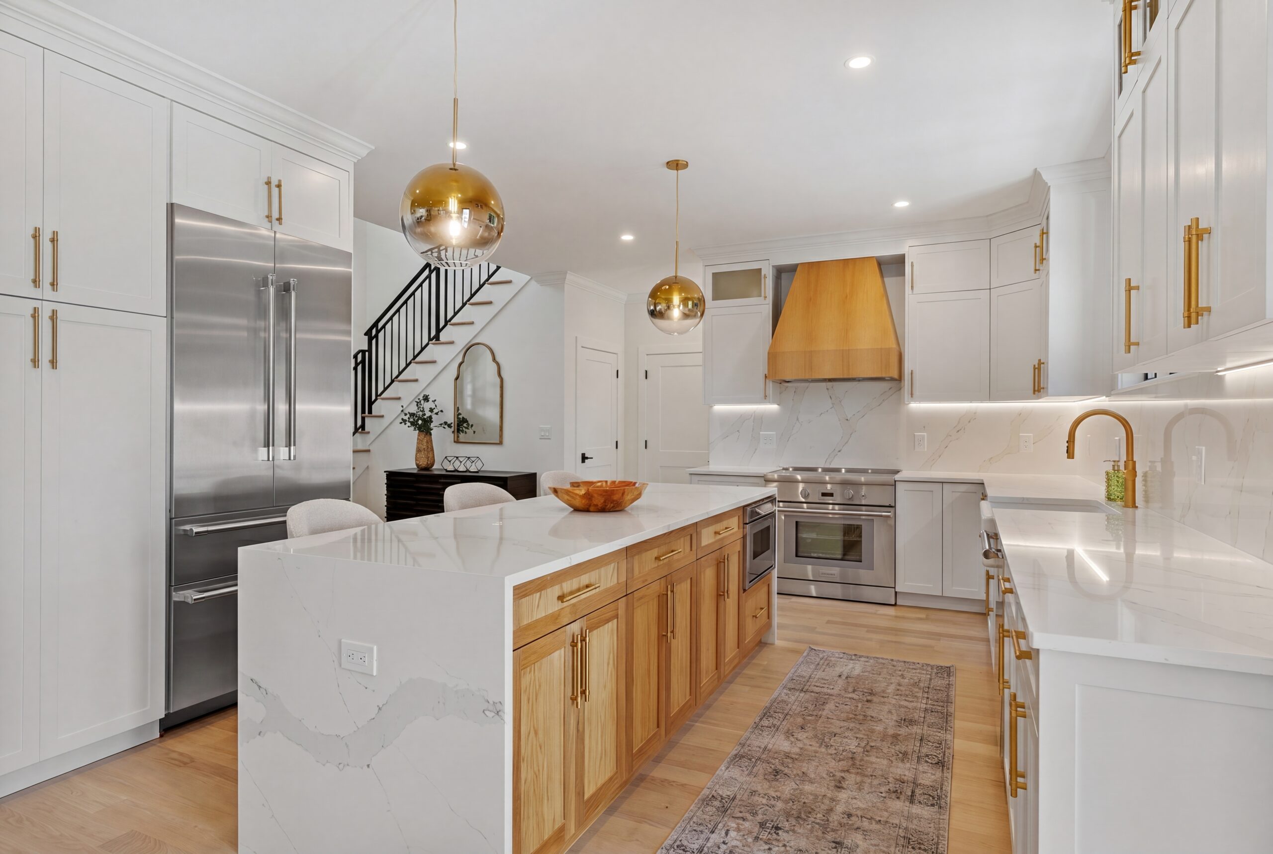 Luxury custom kitchen featuring a waterfall quartz island, white shaker cabinetry, natural wood accents, brass hardware, designer pendant lighting, and premium stainless steel appliances in an open-concept layout.