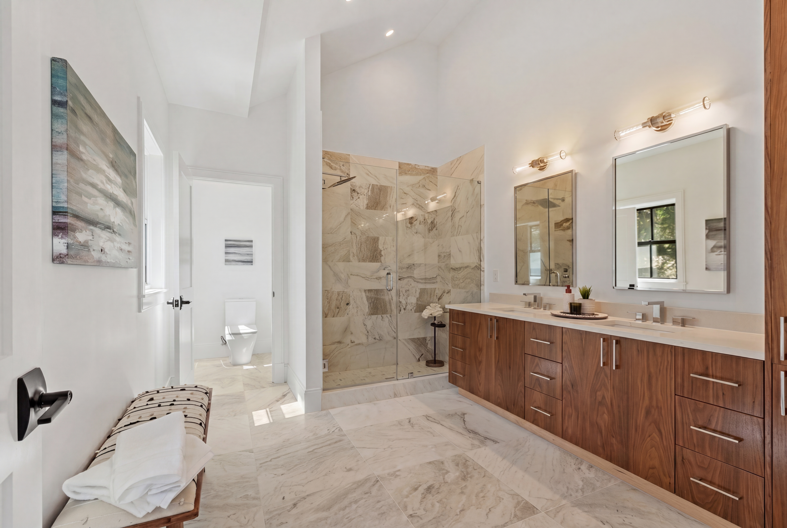 Luxury primary bathroom featuring a double vanity with custom wood cabinetry, marble tile flooring, frameless glass shower, designer lighting, and spa-inspired finishes in a custom single-family residence.