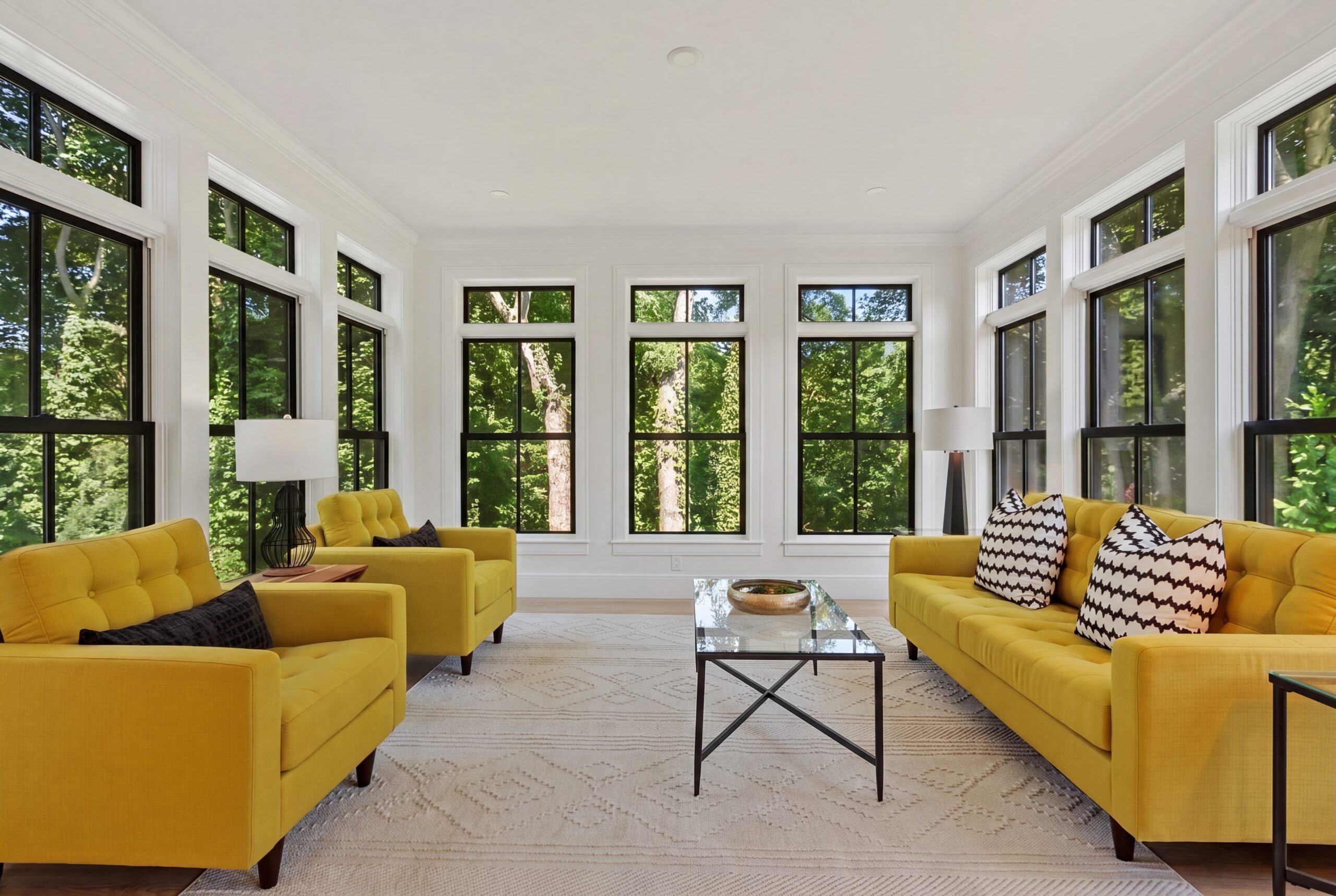 Bright sunroom featuring floor-to-ceiling black-framed windows, abundant natural light, contemporary furnishings, and panoramic views of the surrounding landscape in a luxury single-family residence.
