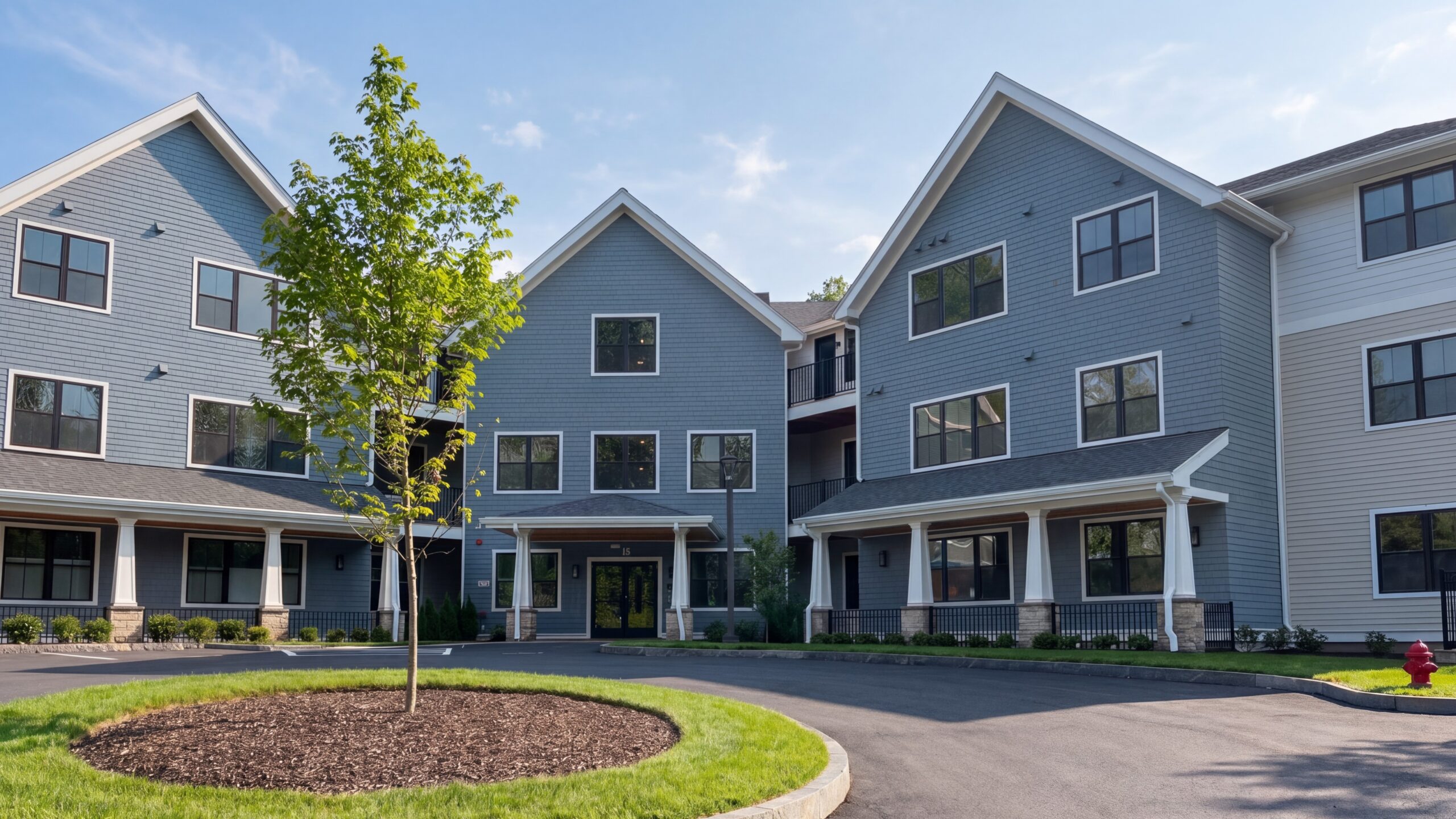 Three-story multi-family building with gabled roofs, covered entries, and landscaped circular drive