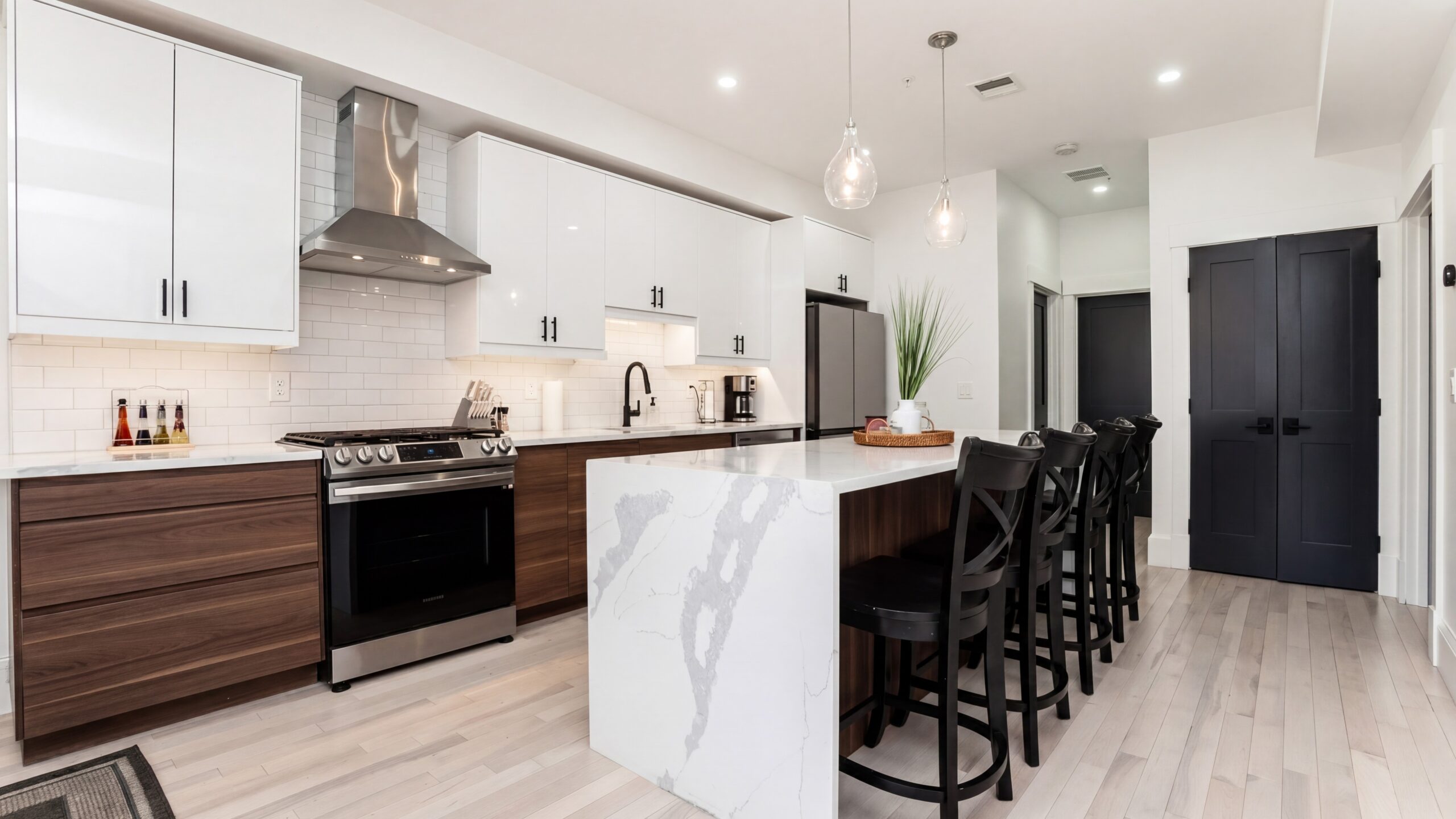 Modern kitchen renovation with waterfall quartz island, custom wood cabinetry, white upper cabinets, and contemporary black accents.