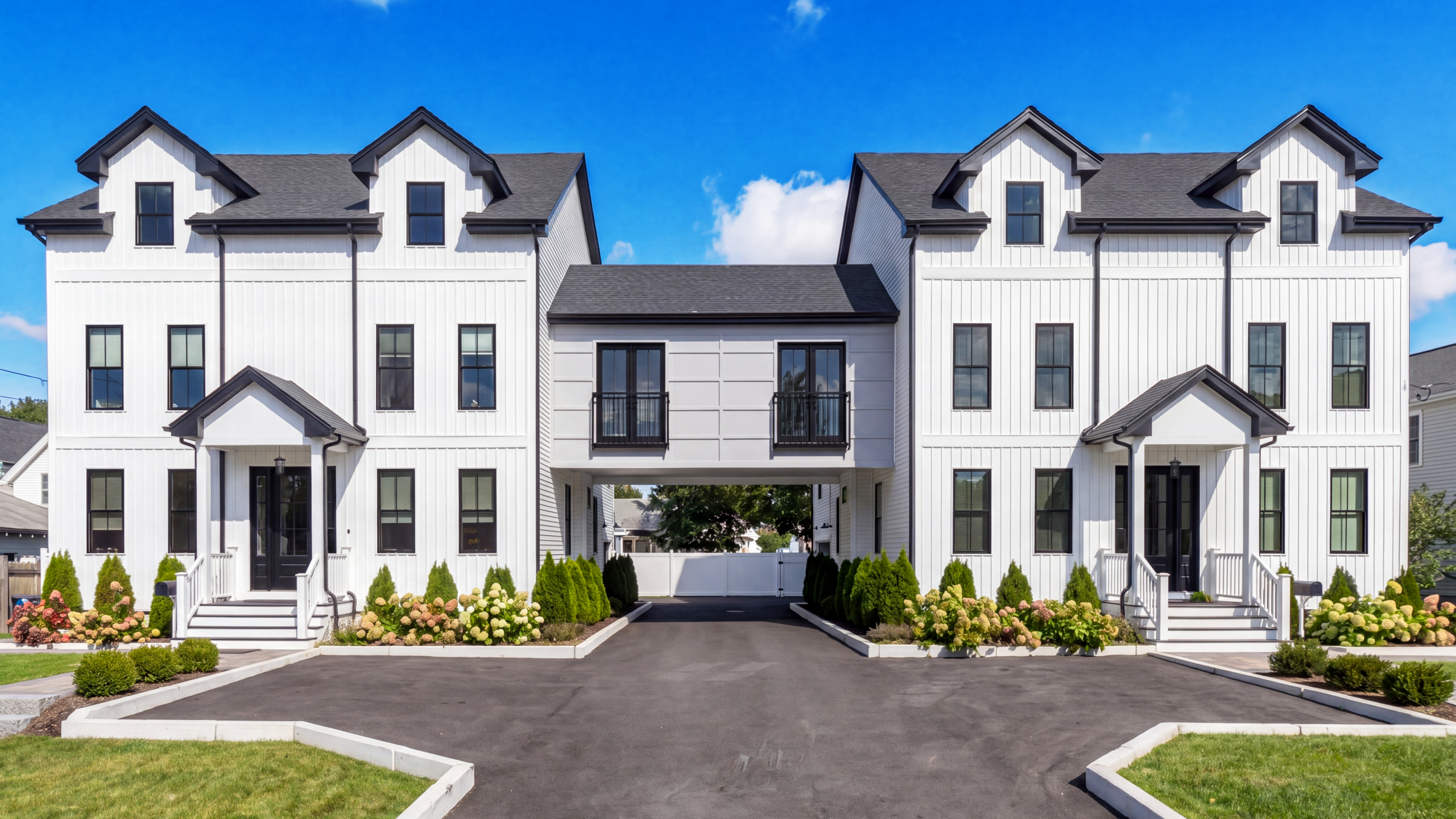 Symmetrical modern farmhouse duplex with white vertical siding, black windows, central breezeway connection, and landscaped front entries along shared driveway