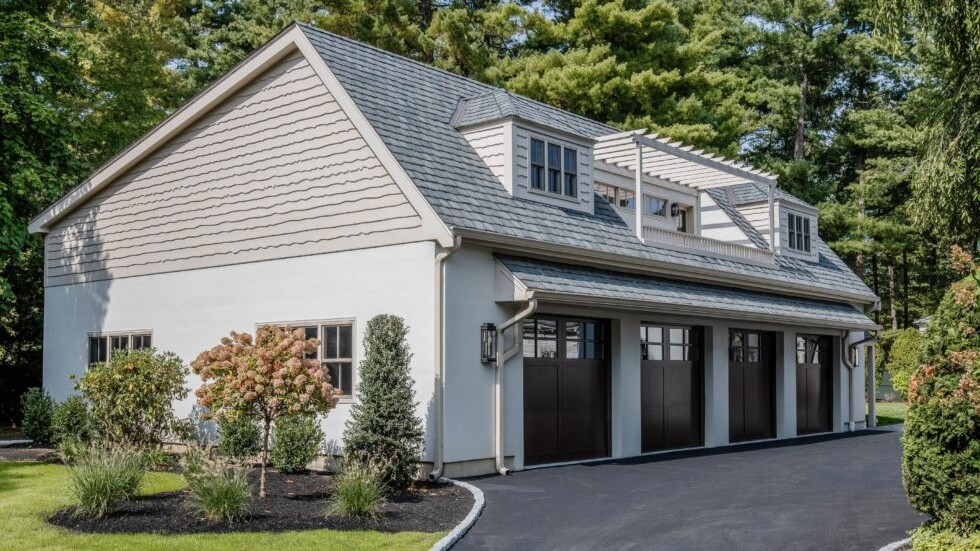Coastal-inspired detached garage and guest house with gambrel rooflines, pergola terrace, and carriage-style garage doors surrounded by landscaped grounds