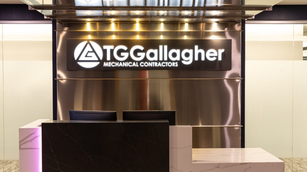 Modern reception desk with marble finishes and illuminated TG Gallagher Mechanical Contractors sign on metal backdrop