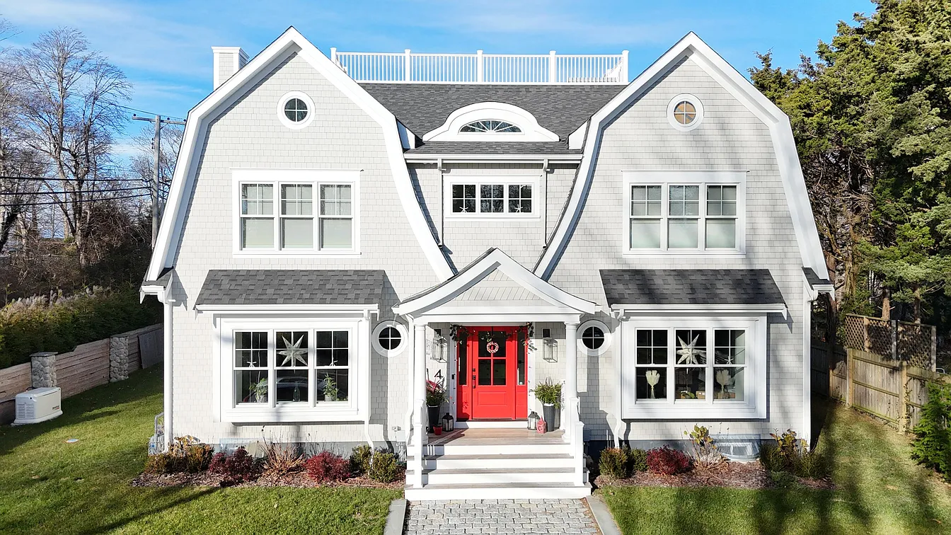 Coastal-inspired single-family home with gambrel roofs, rooftop deck, and symmetrical shingle-style façade featuring a bold red entry door