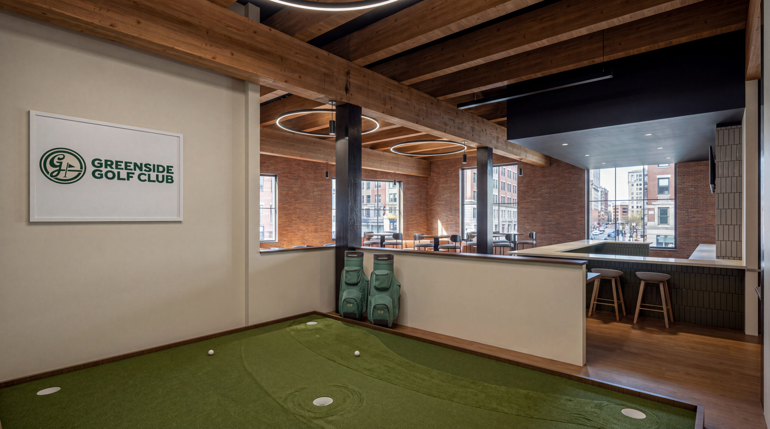Interior rendering of Greenside Golf Club featuring an indoor putting green, golf bags, and an adjacent bar beneath exposed timber beams and circular pendant lights.